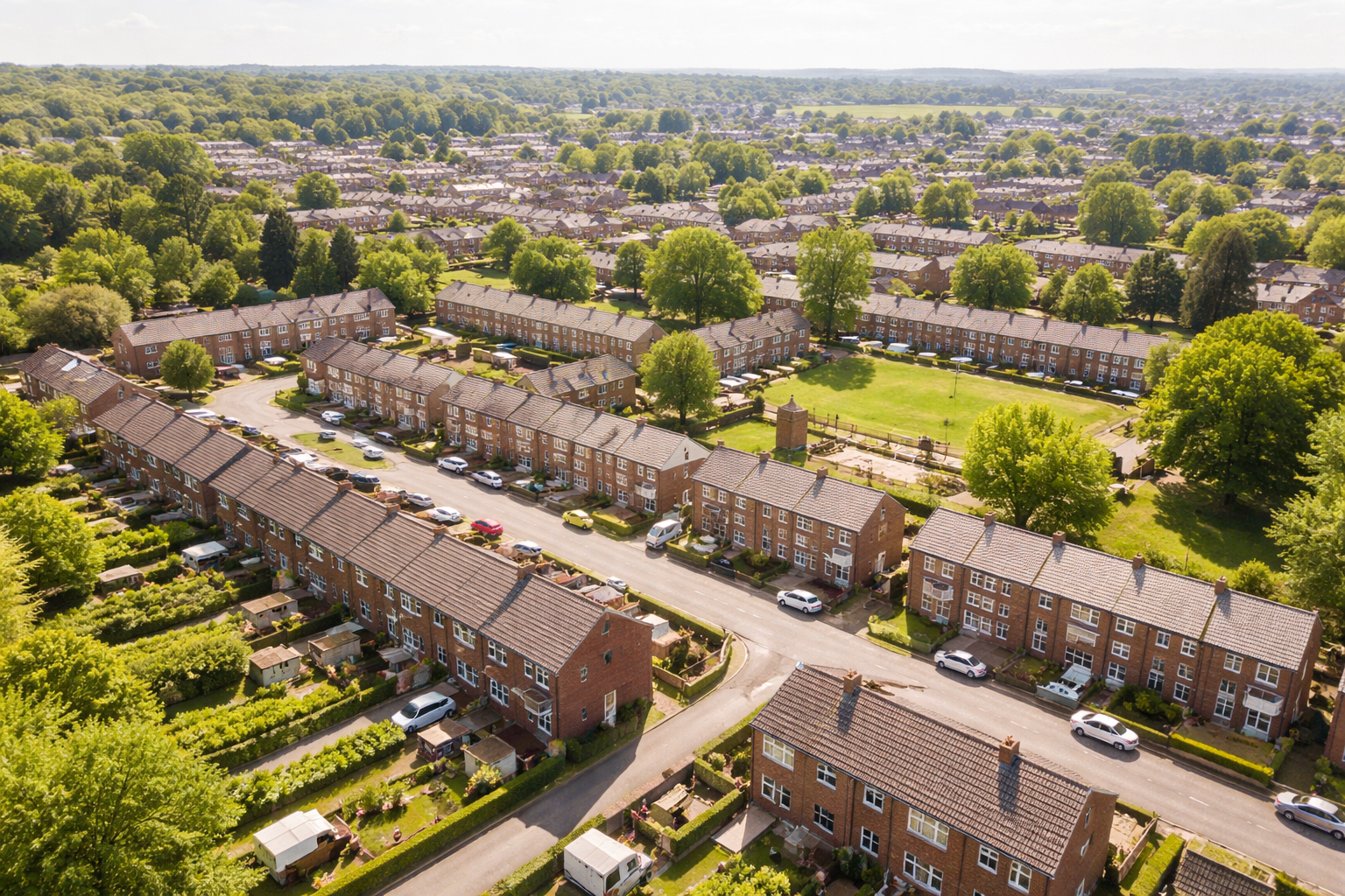 Aerial view of a suburban neighborhood with brick houses, green trees, and a park, under a partly cloudy sky.