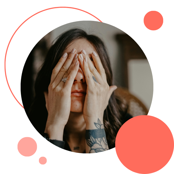 A person covers their face with both hands, wearing rings and showing a tattoo.