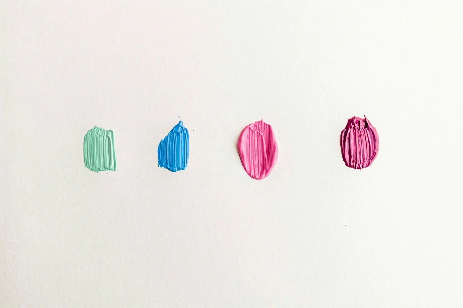 Four paint swatches in green, blue, pink, and purple are evenly spaced on a white background. Each swatch has a textured, brushstroke appearance.