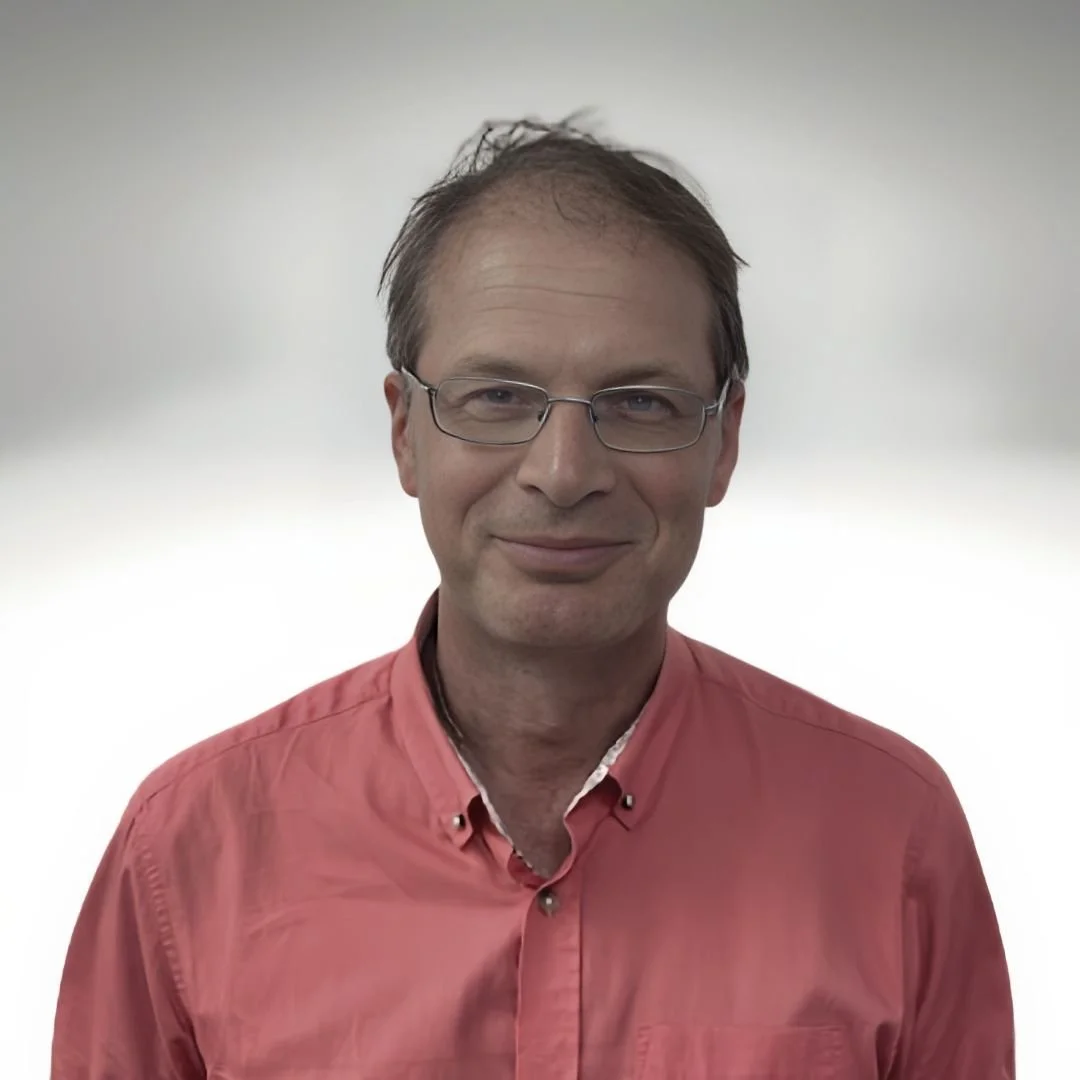 Portrait of a man with glasses wearing a pink button-up shirt smiling at the camera.
