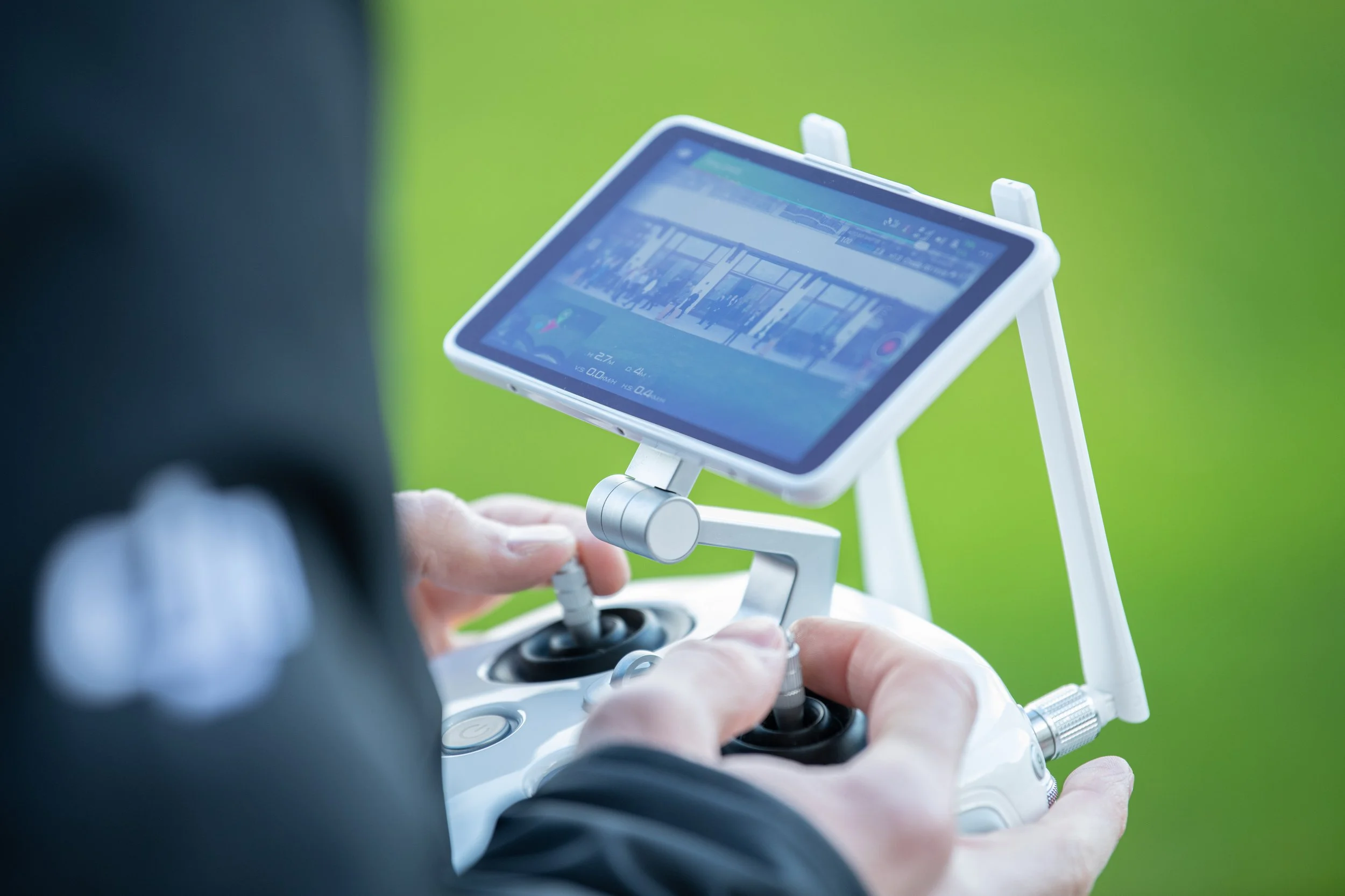Une personne utilisant une radiocommande avec un écran, probablement pour piloter un drone, devant un fond vert.