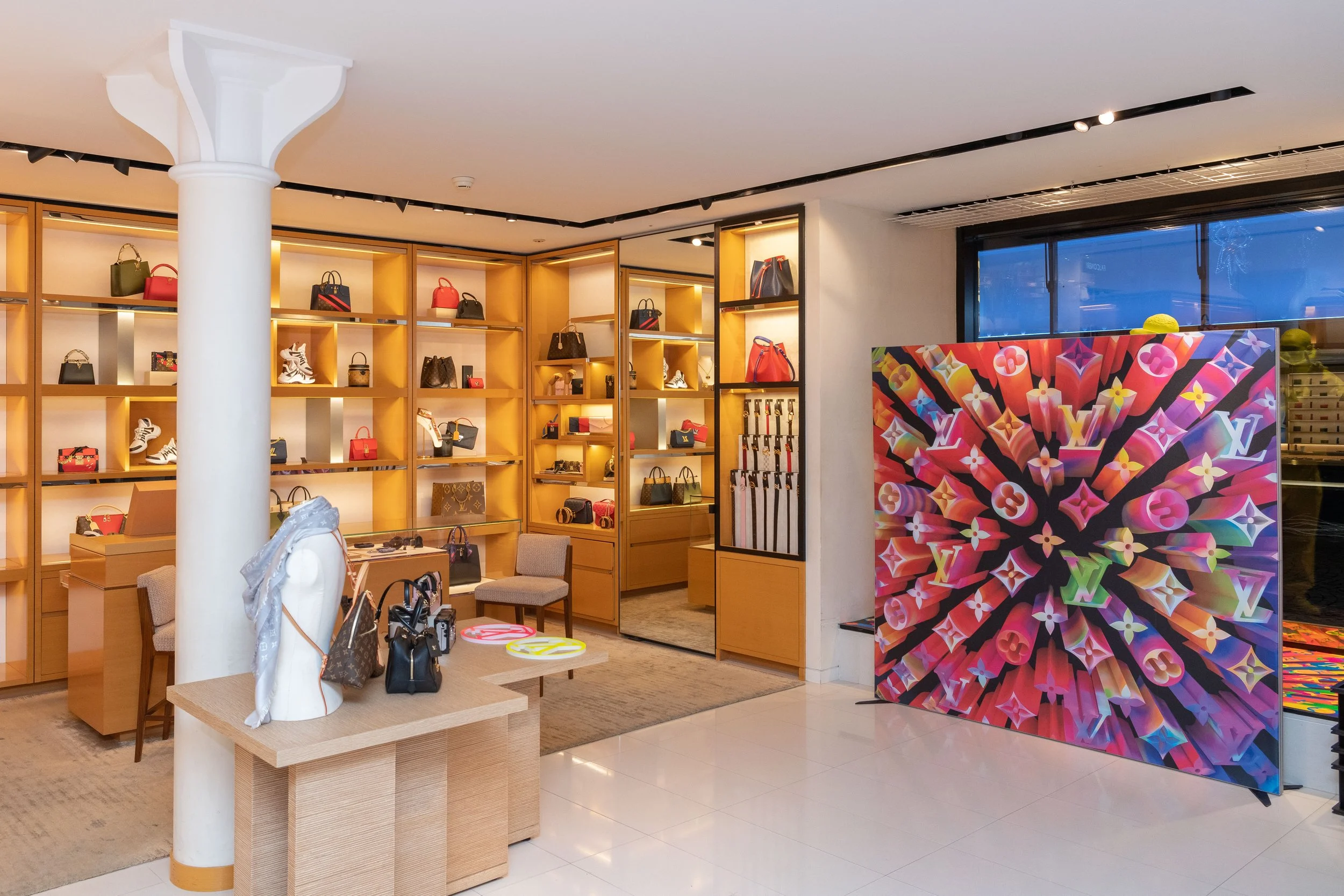 Boutique de luxe avec étagères en bois remplies de sacs à main, chaussures et accessoires, devant une grande affiche colorée de Louis Vuitton