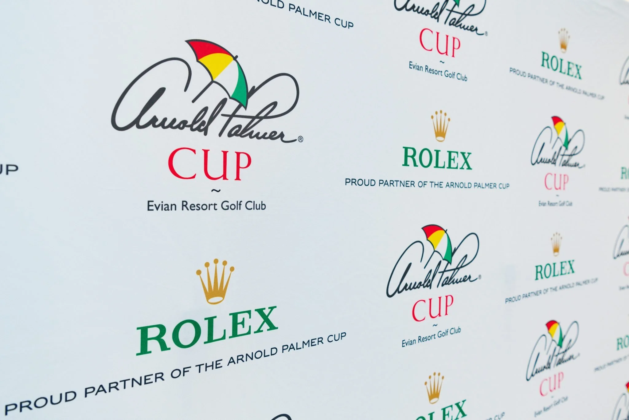 Logos de sponsors de la compétition Arnold Palmer Cup, incluant Rolex et Evian Resort Golf Club, sur une affiche.