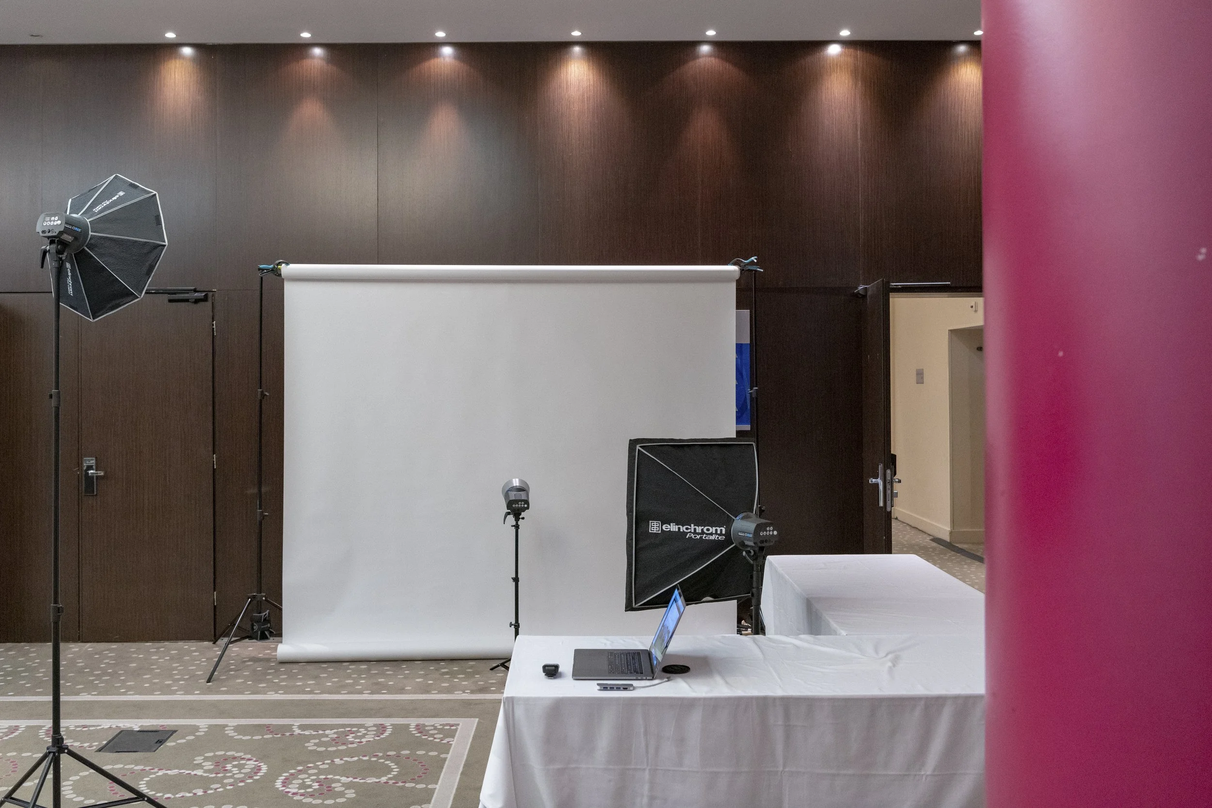 Configuration de studio photo avec panneau blanc, éclairages, ordinateur portable sur une table, et un mur en bois sombre en arrière-plan.
