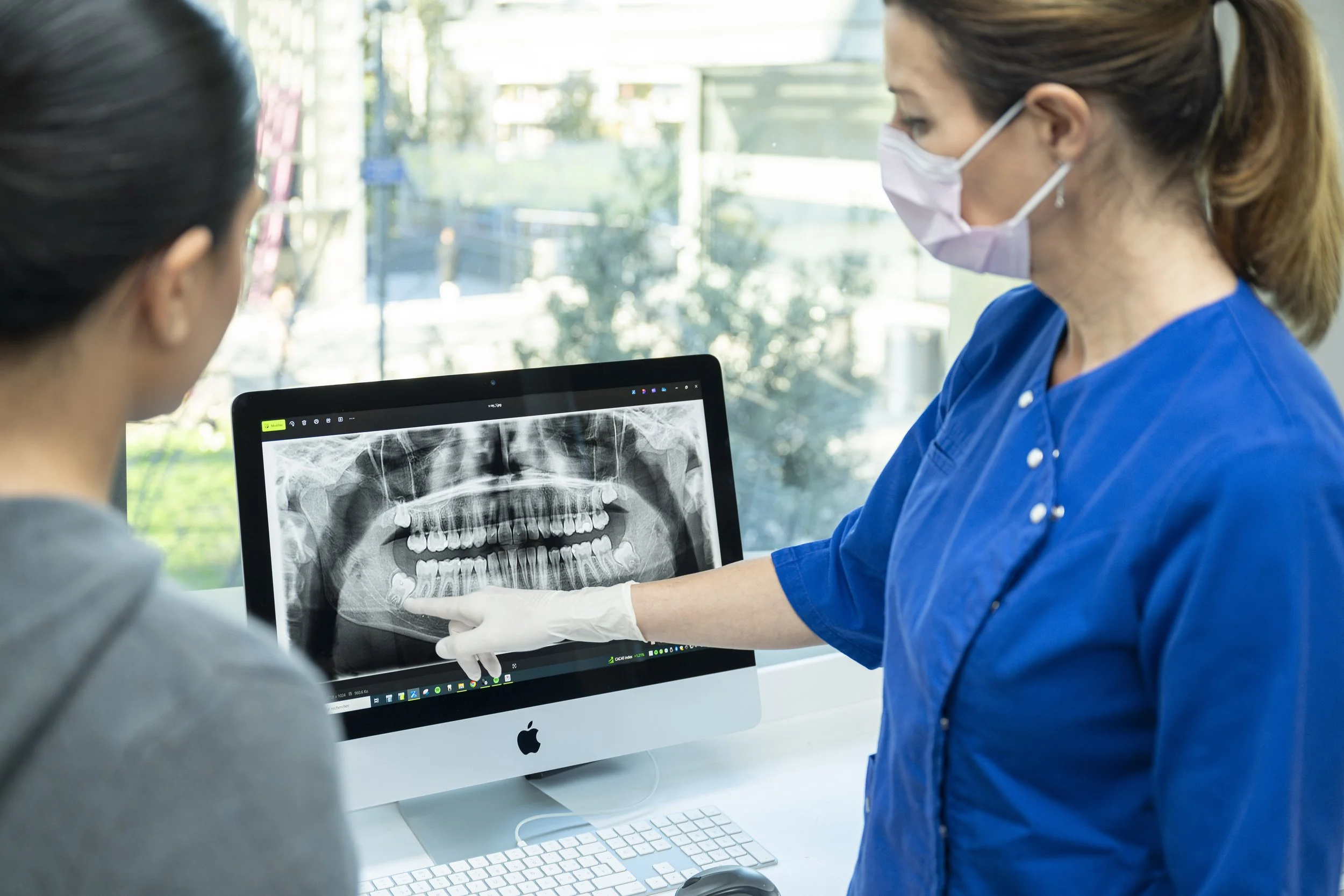 Une dentiste discutant avec un patient, pointant une radiographie dentaire affichée sur un ordinateur, dans un environnement de clinique dentaire moderne