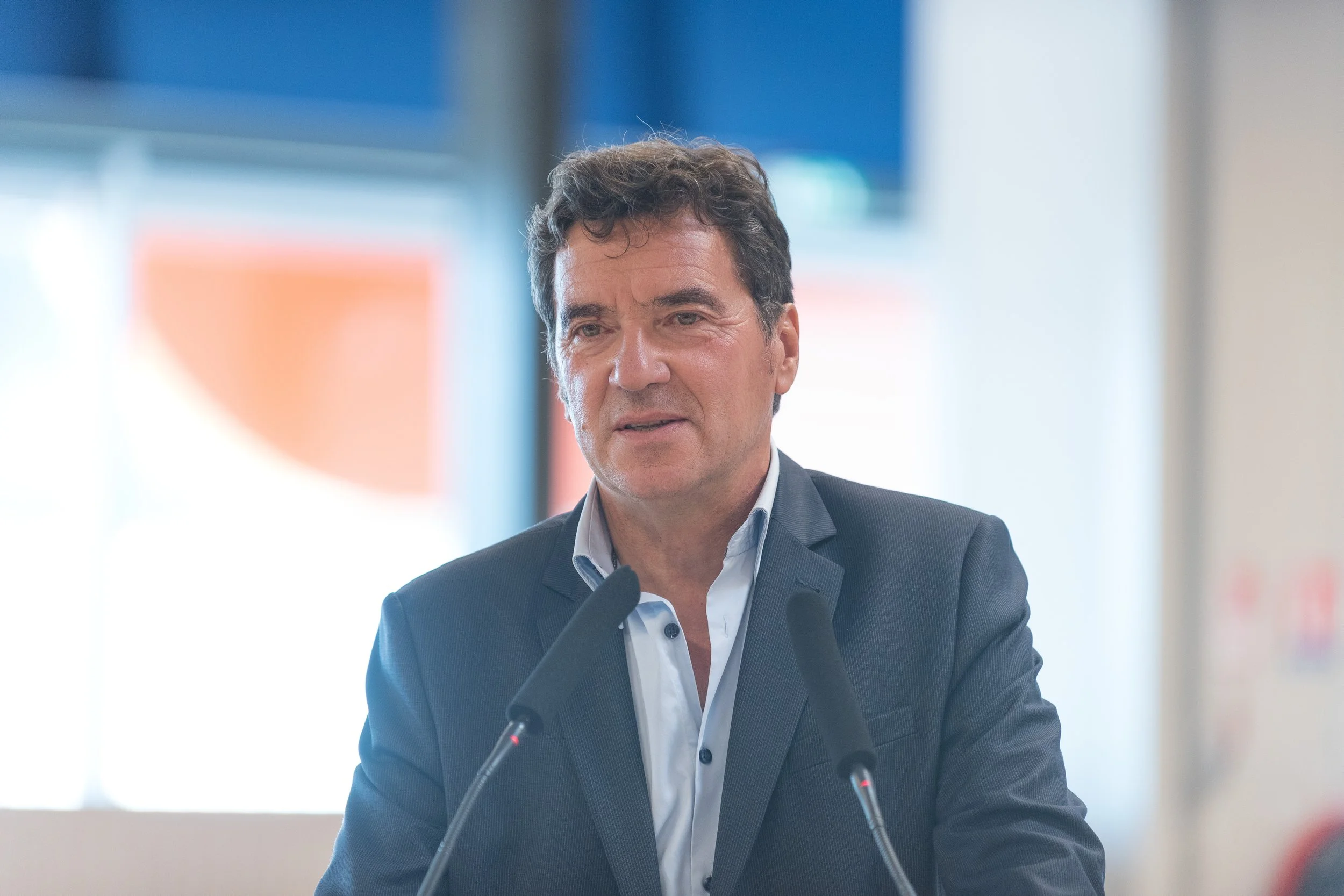 Un homme d'affaires parle lors d'une conférence avec deux microphones sur un fond flou.