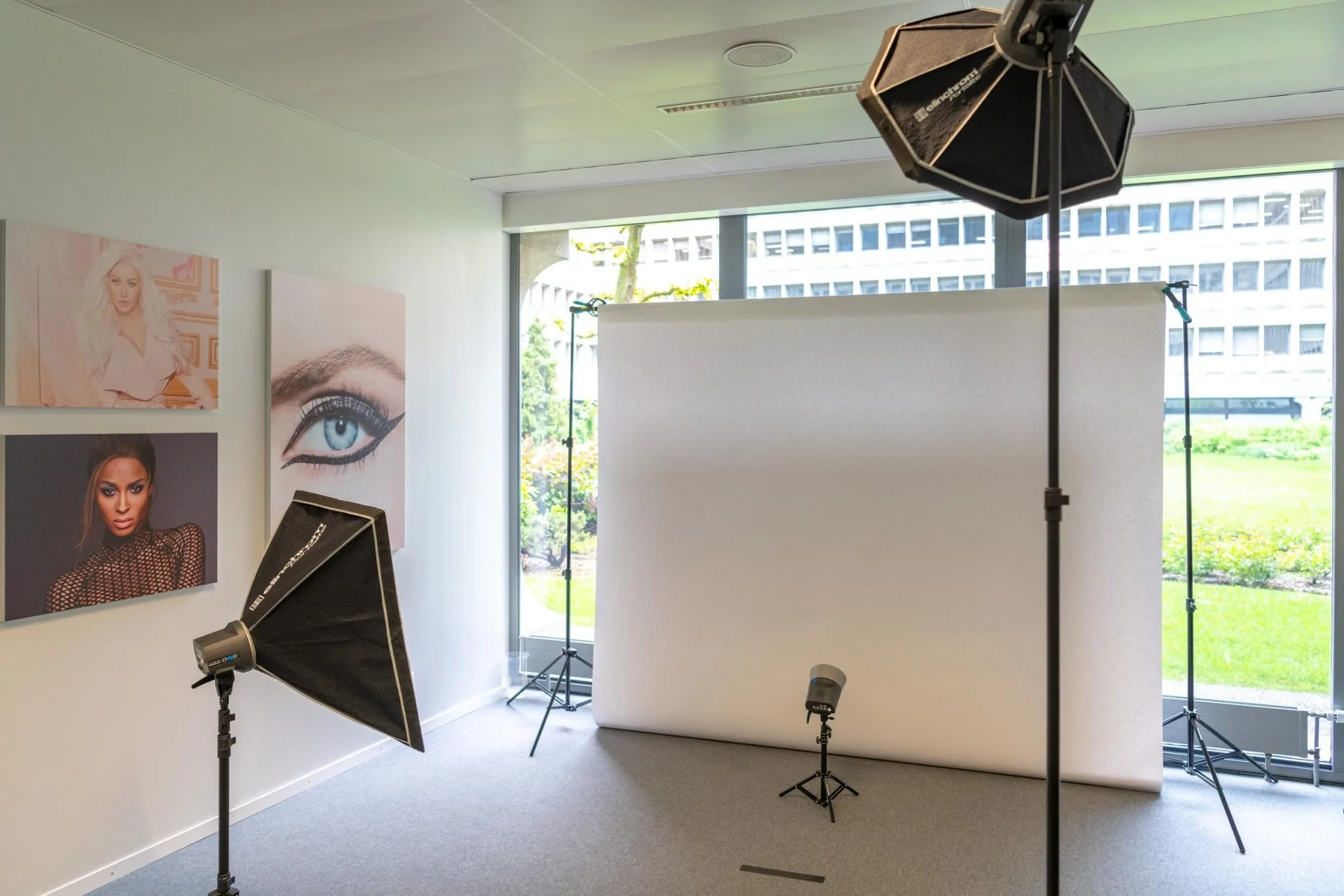 Studio photographique avec éclairages, toile de fond blanche, et œuvres d'art de portraits féminins sur le mur.