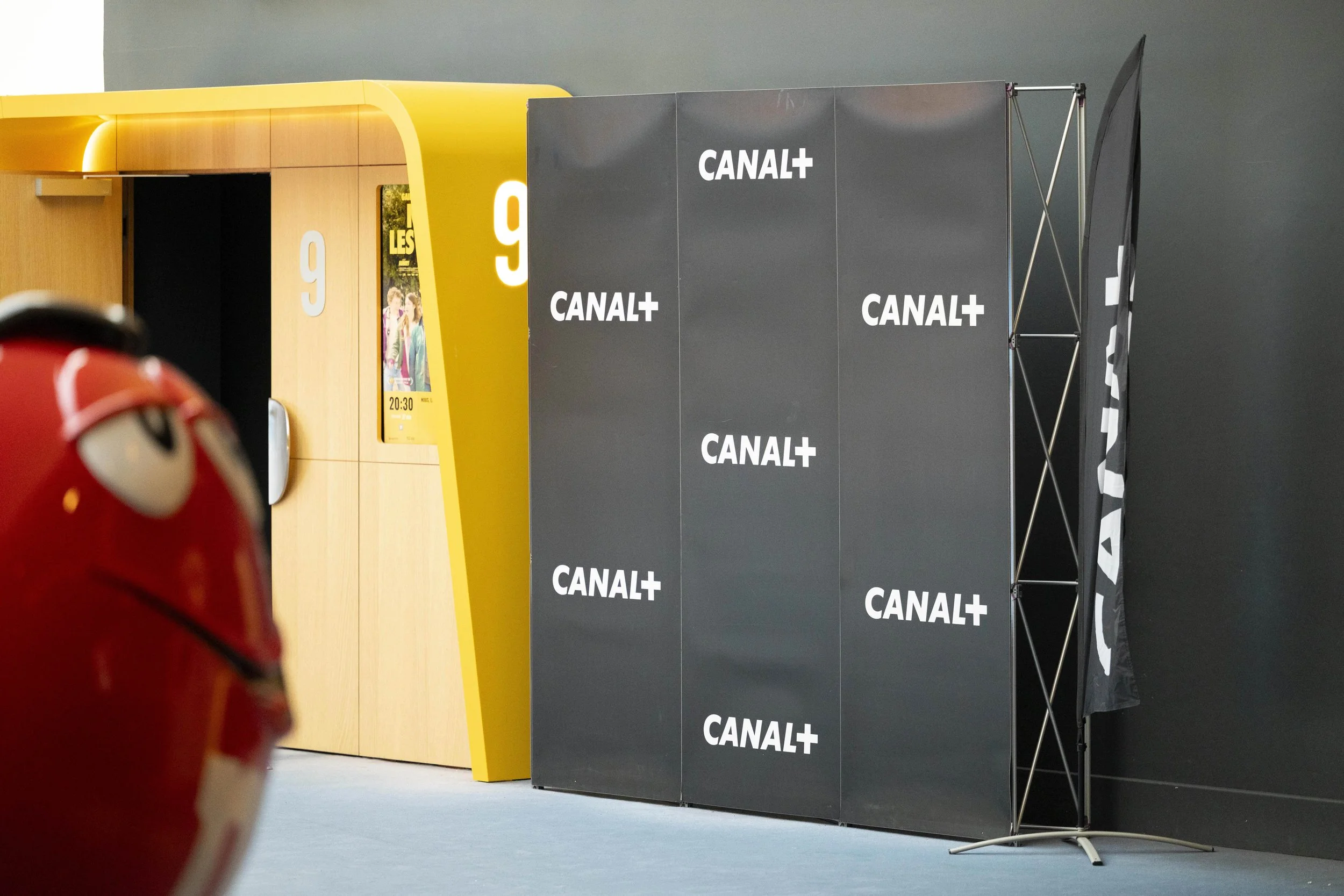 Partie intérieure d'une station, avec un mobilier jaune et une structure noire avec le logo CANAL+ répété.