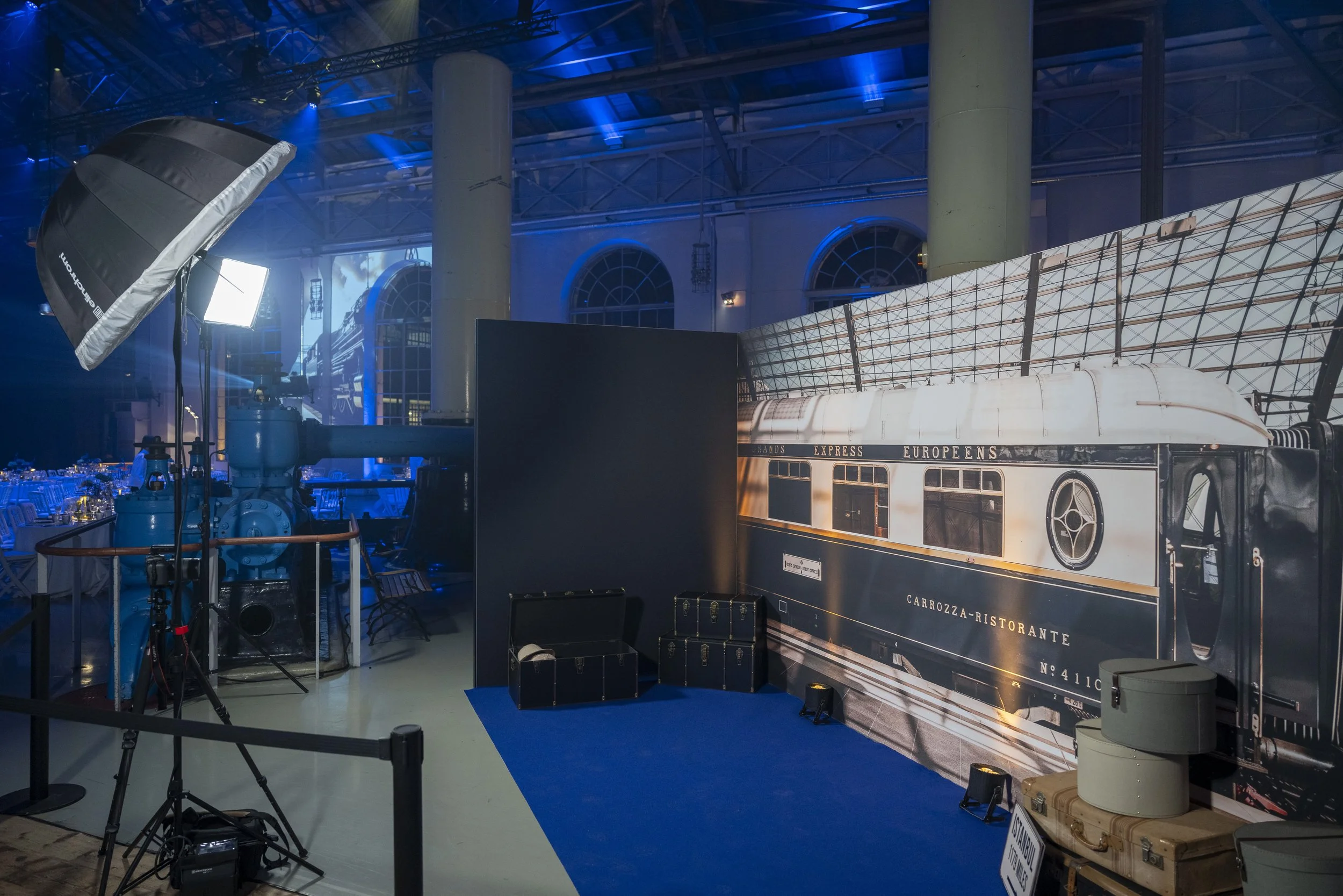 Une scène d'un événement où un décor représentant un ancien wagon de train est visible, avec des éclairages professionnels, du matériel de photographie et des tables de banquet en arrière-plan.