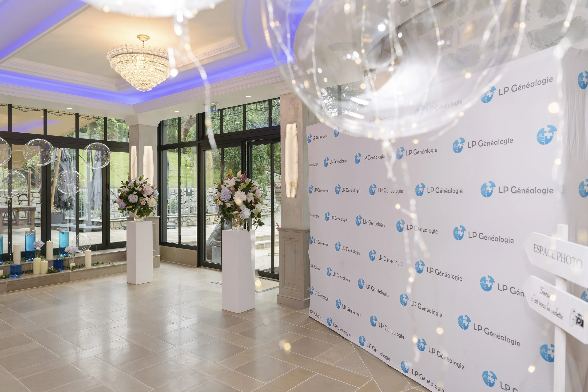 Intérieur élégant avec chandelle, grandes fenêtres et décor floral pour une célébration ou un événement, avec un panneau de fond LP Généalogie.