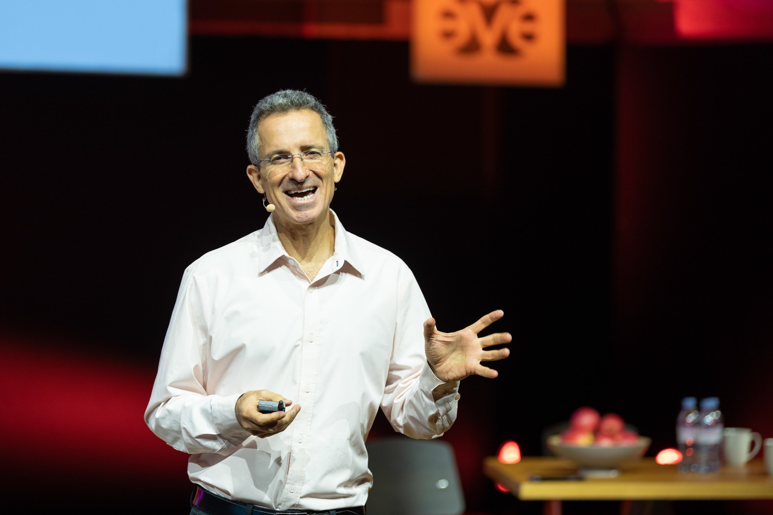Un homme souriant porte un micro et un pointeur lors d'une présentation ou conférence.