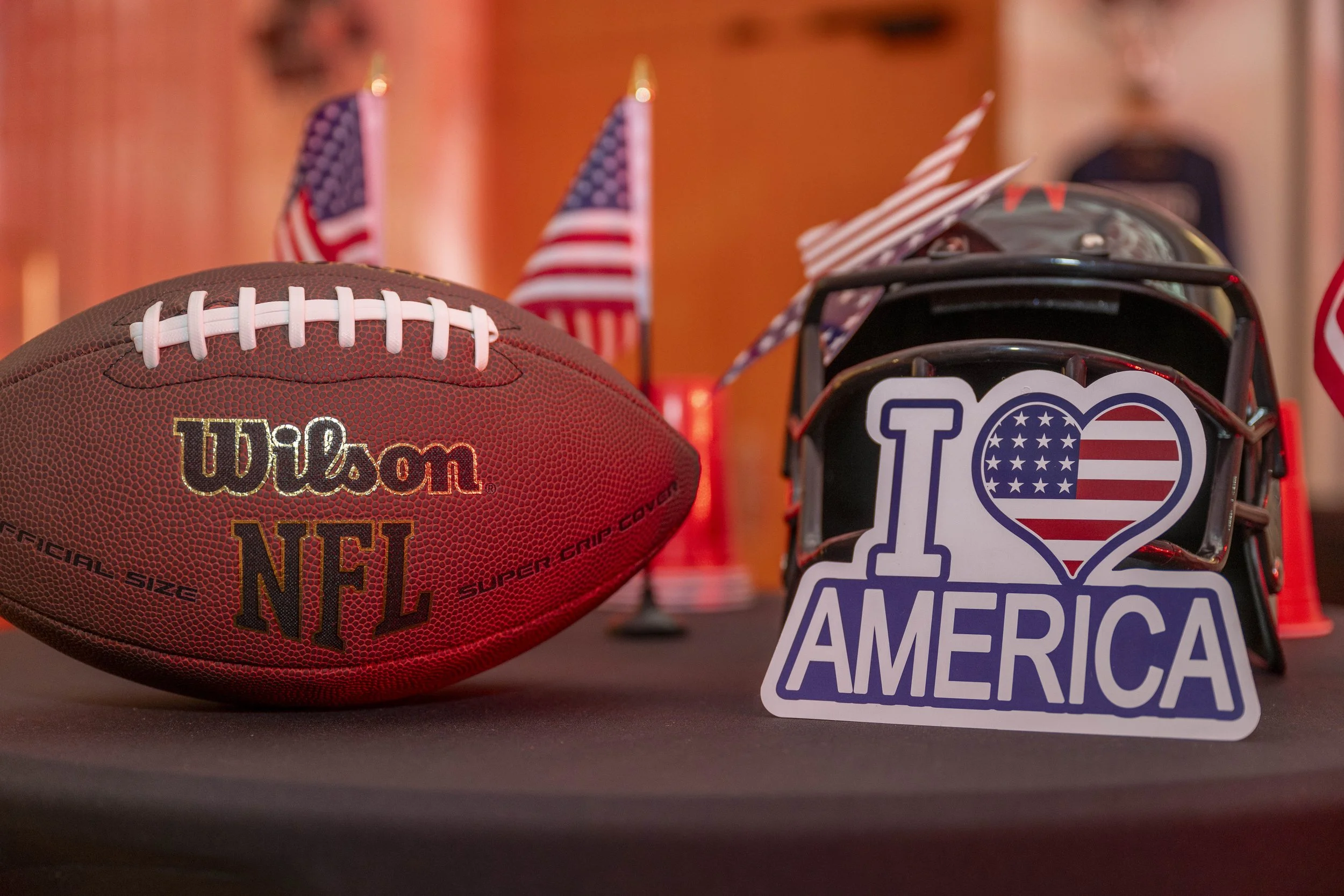 Ballon de football de la NFL, casque de football américain avec un sticker 'I Love America', et petites drapeaux américains en arrière-plan.