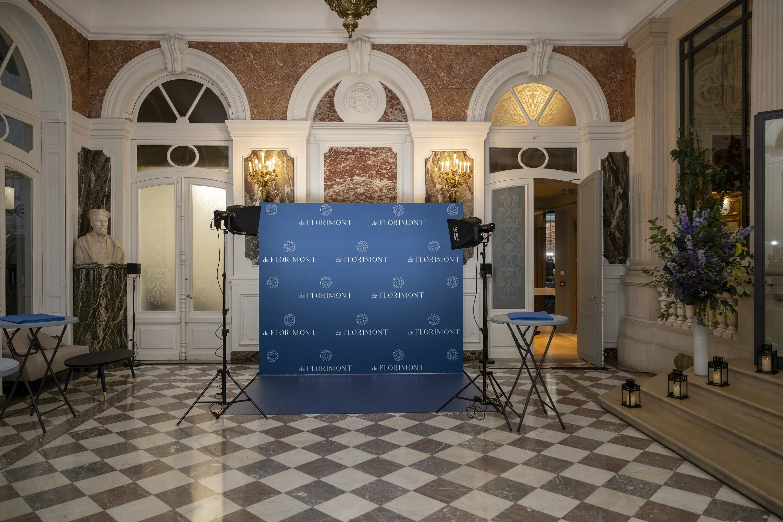 Intérieur élégant avec un mur en marbre, un bustes en marbre, une grande plante avec des fleurs violettes, et un panneau de fond bleu marqué 'de FLORIMONT'.