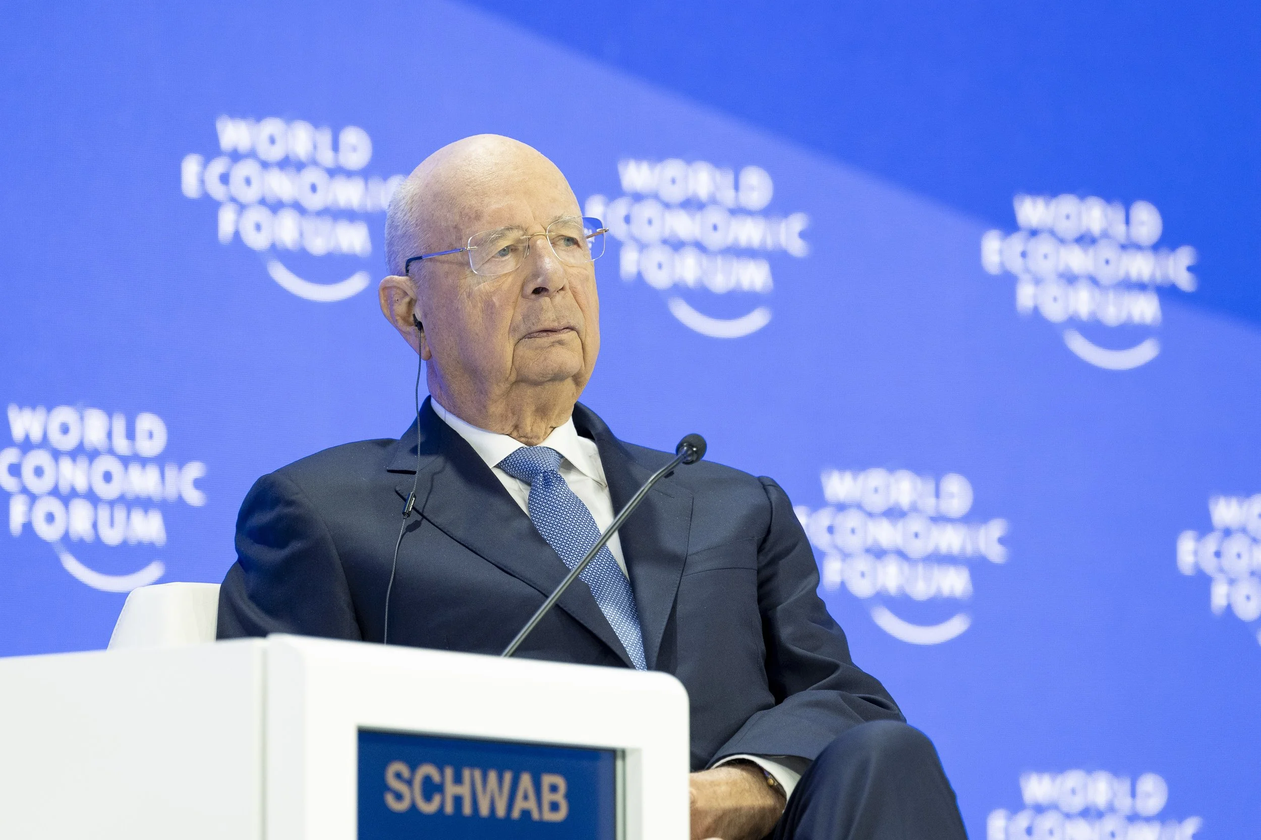 Un homme âgé en costume sombre, portant des lunettes, assis lors d'une conférence du Forum économique mondial.