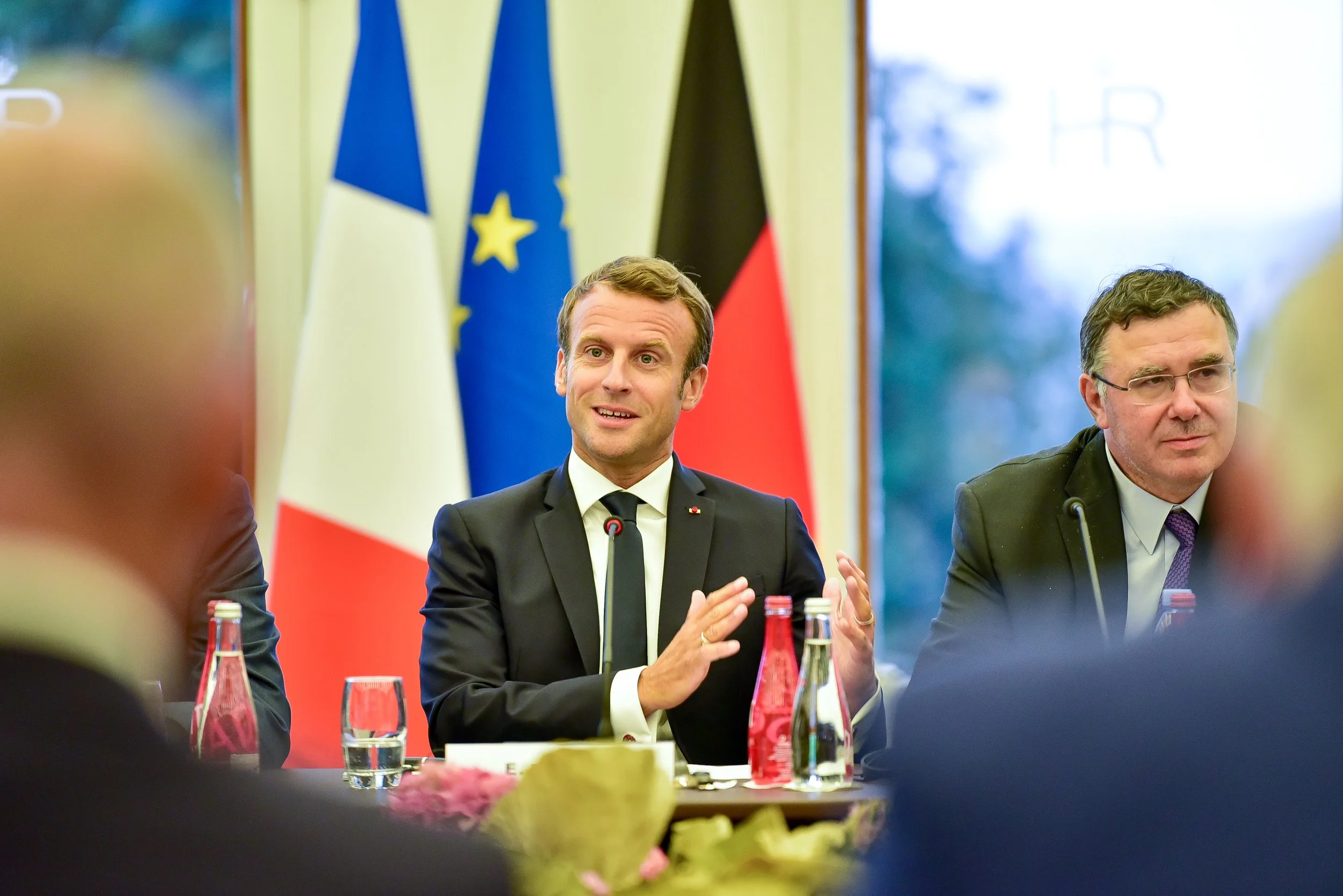Emmanuel Macron lors d'une réunion officielle avec des drapeaux français, européen et allemand en arrière-plan.