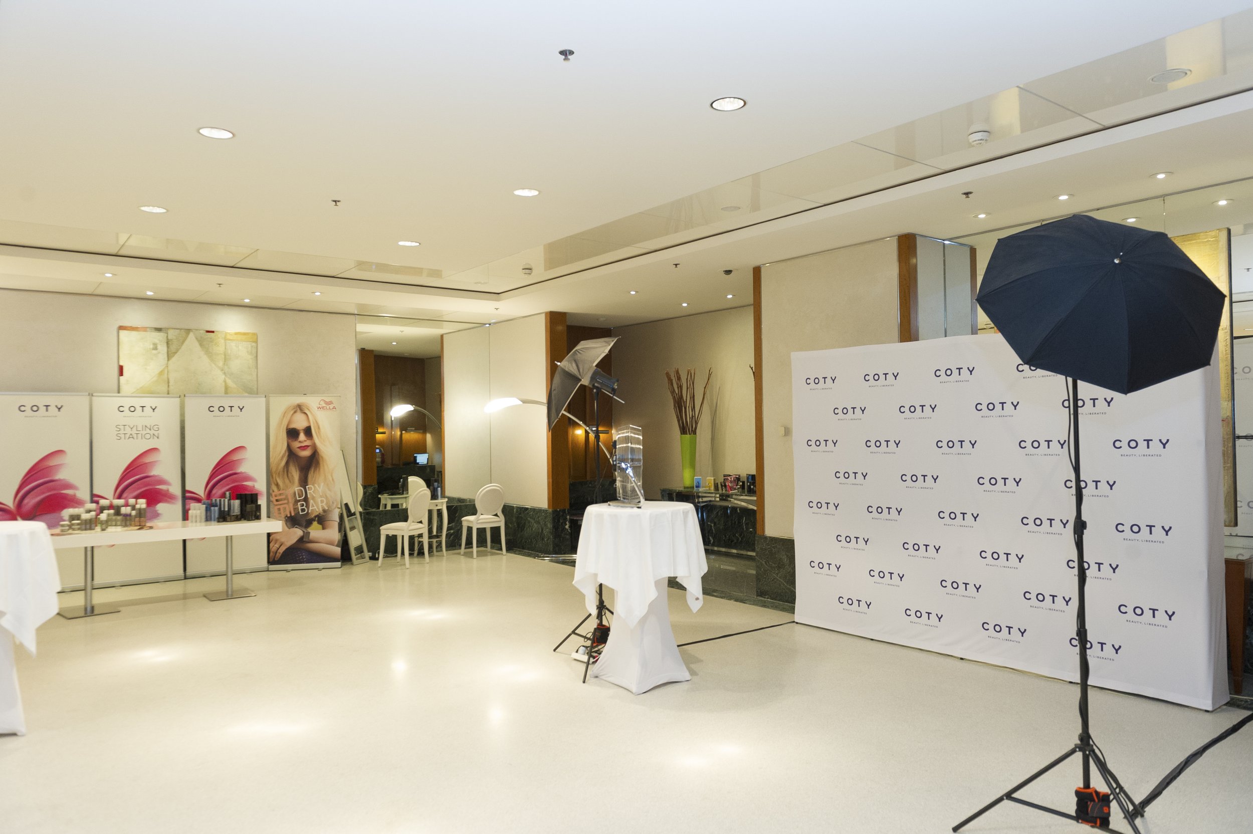 Espace intérieur de salon de coiffure ou de beauté, avec écrans de publicité pour produits capillaires, tables avec produits, équipement de studio photo avec éclairage et fond personnalisé.