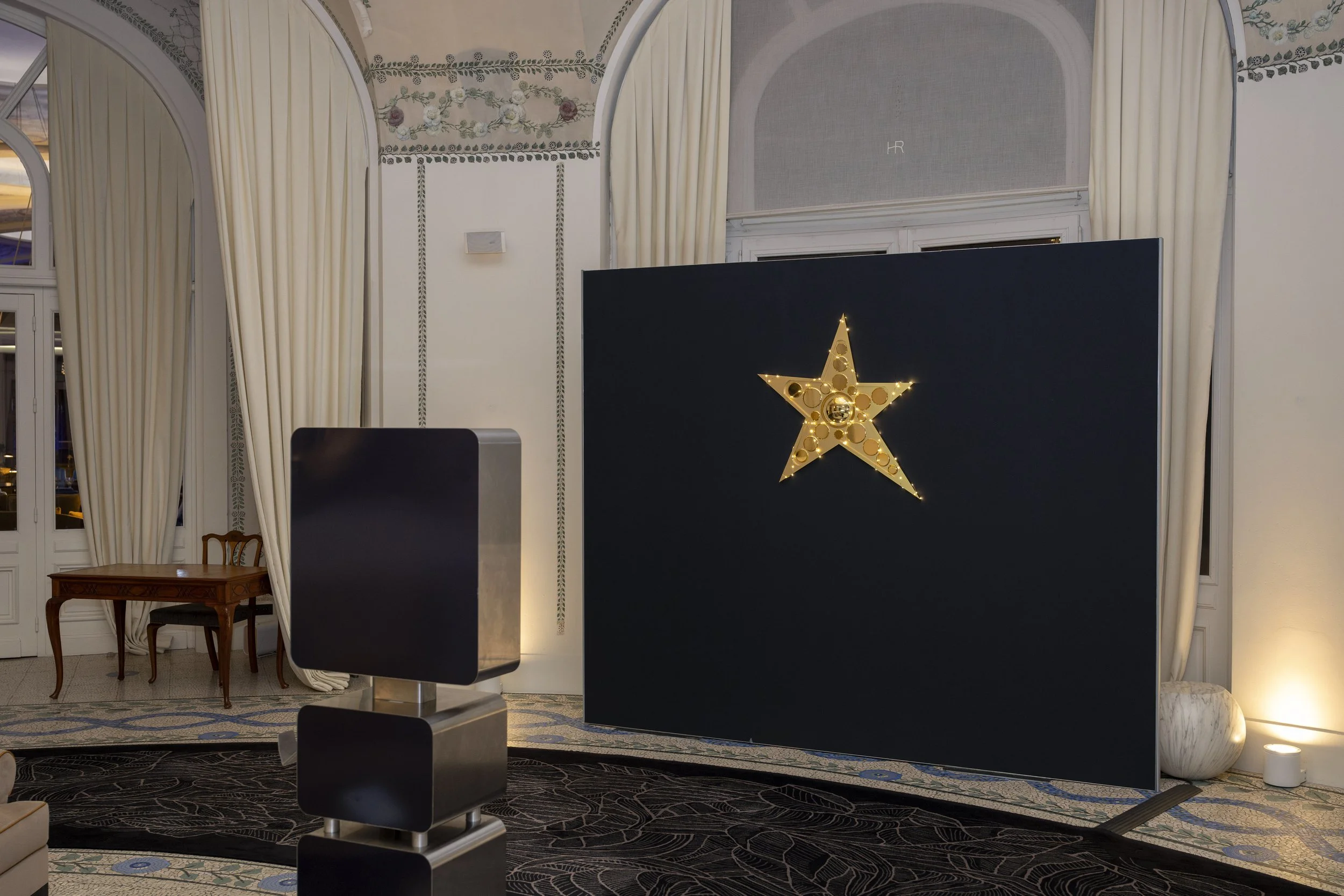 Décor intérieur élégant avec un panneau noirorné d'une étoile dorée illuminée, rideaux blancs, table en bois, meubles en marbre et tatami. Idéal pour une réception ou un événement.
