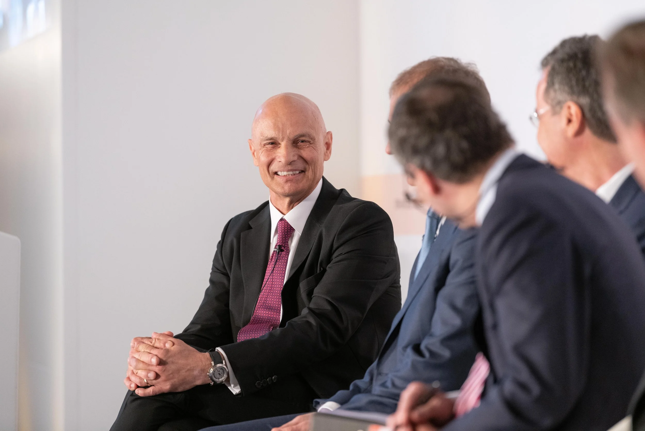 Un homme d'affaires souriant lors d'une réunion avec plusieurs autres hommes en costume dans une salle de conférence.