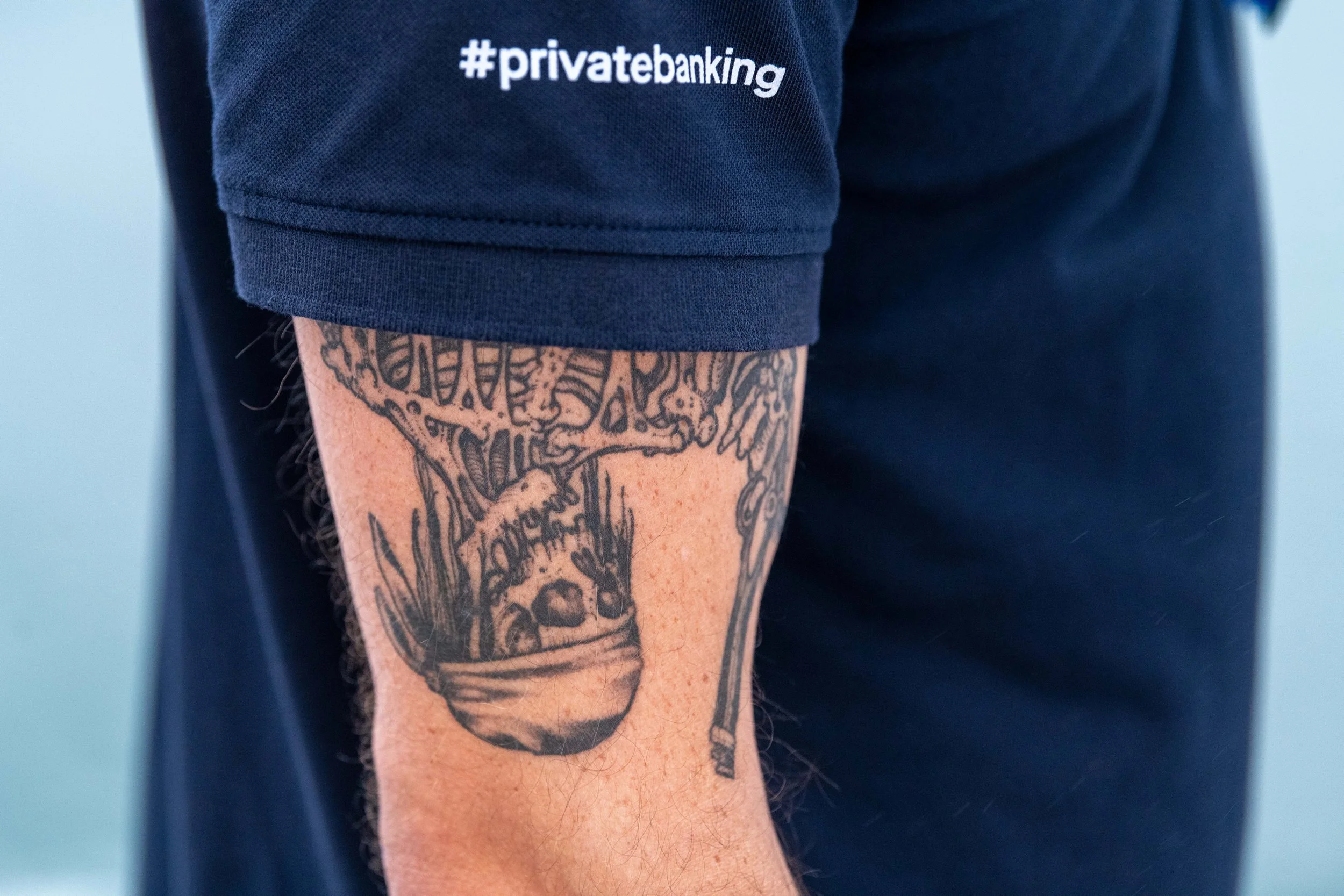 Tatouage d'un bol de ramen avec des baguettes sur le bras d'une personne portant un sweatshirt avec le hashtag #privatebanking.