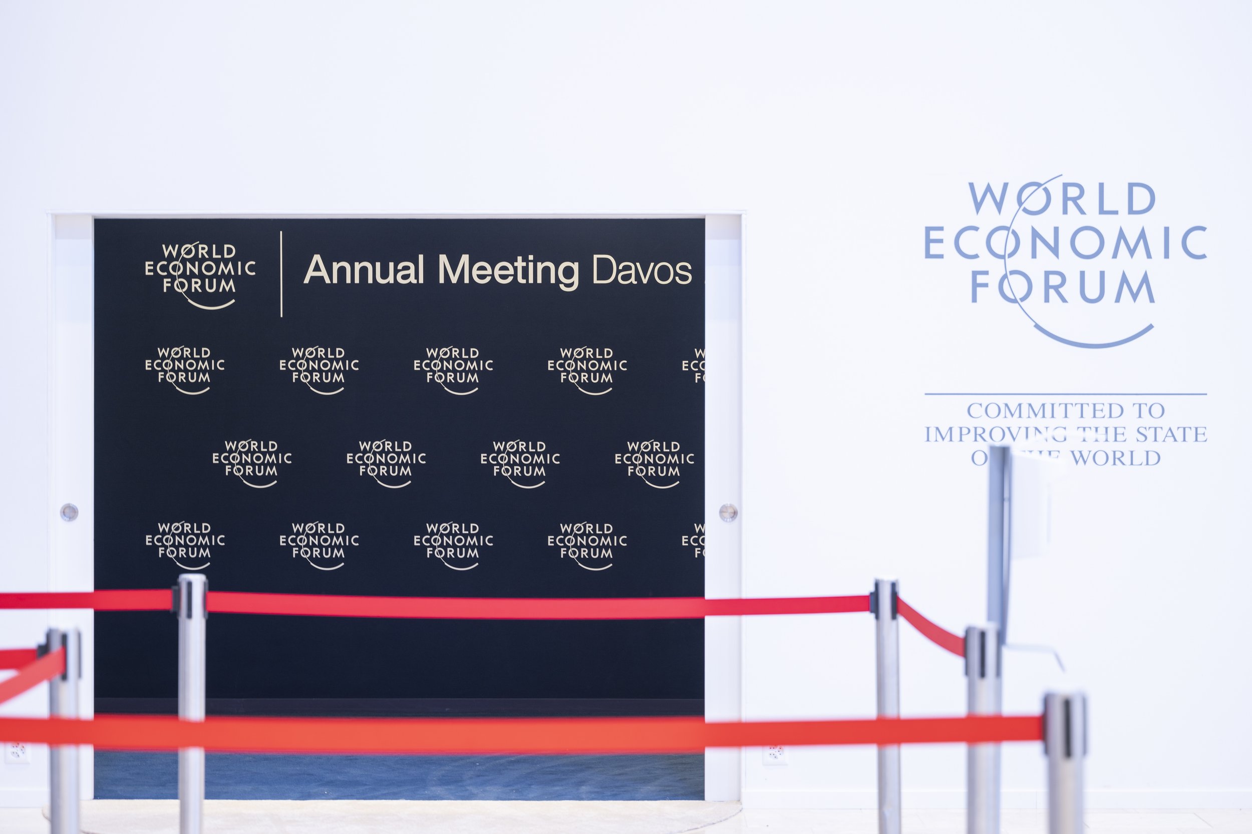 Entrée avec panneau indiquant la réunion annuelle du Forum Économique Mondial à Davos, entourée de barriers rouges.