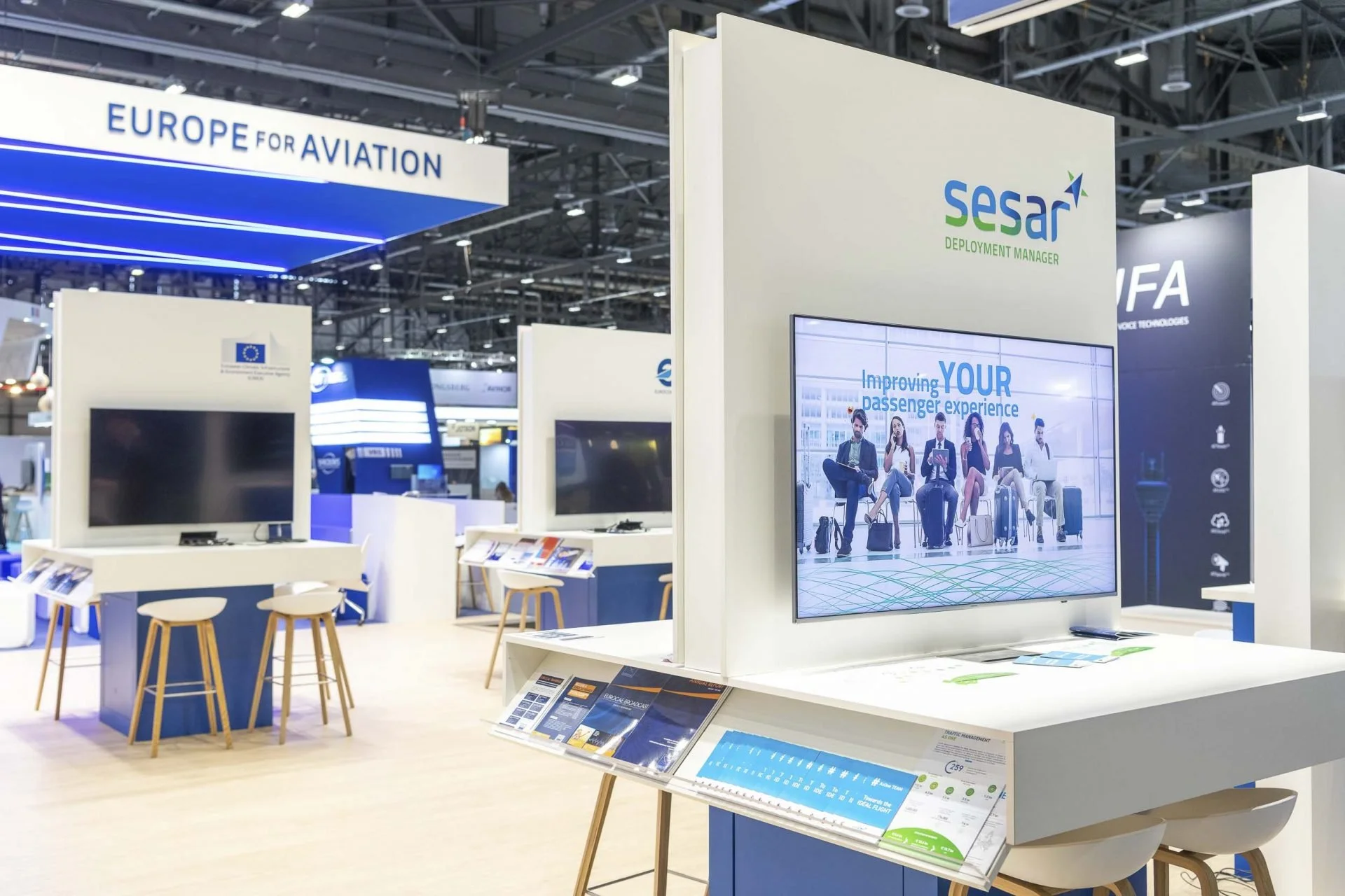 Stands d'exposition avec écrans et brochures dans un salon aéronautique européen, promotion de solutions pour améliorer l’expérience passager.