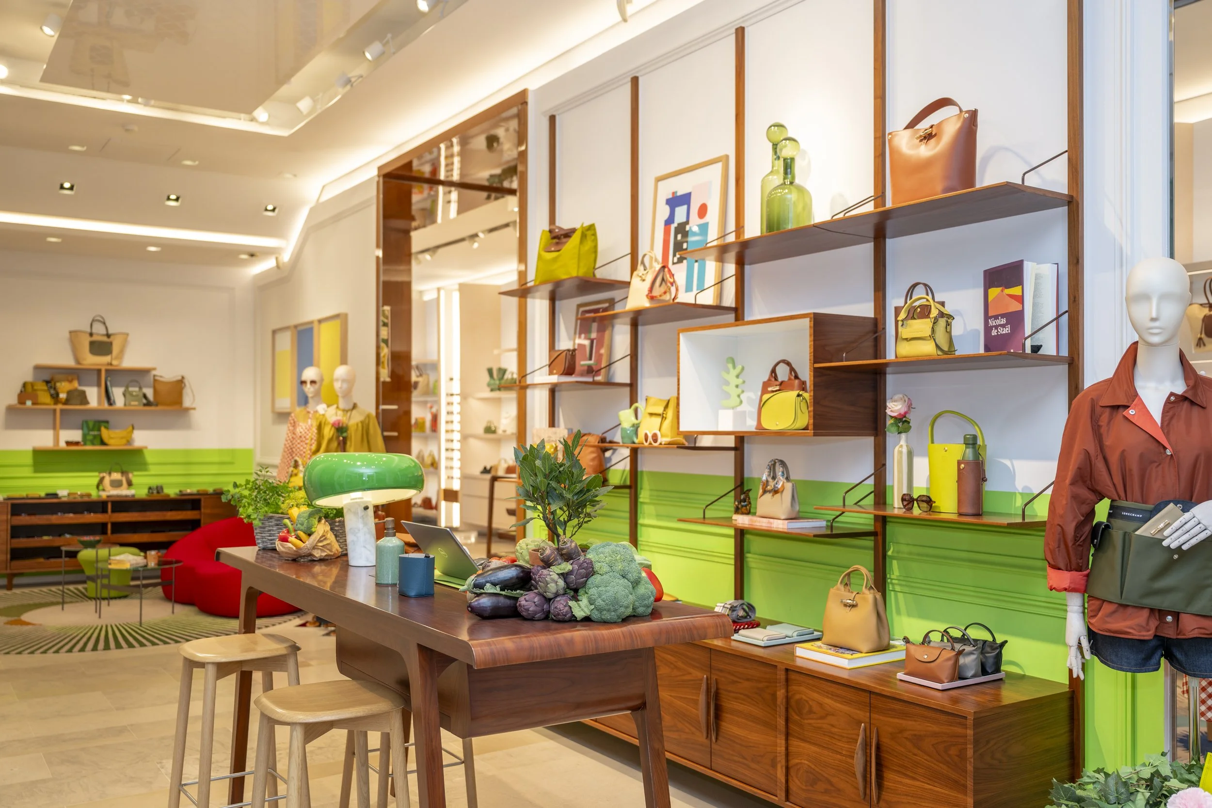 Intérieur d'une boutique de mode avec des mannequins en vitrine, étagères avec des sacs à main colorés, une table avec des légumes décoratifs, et un éclairage chaleureux.