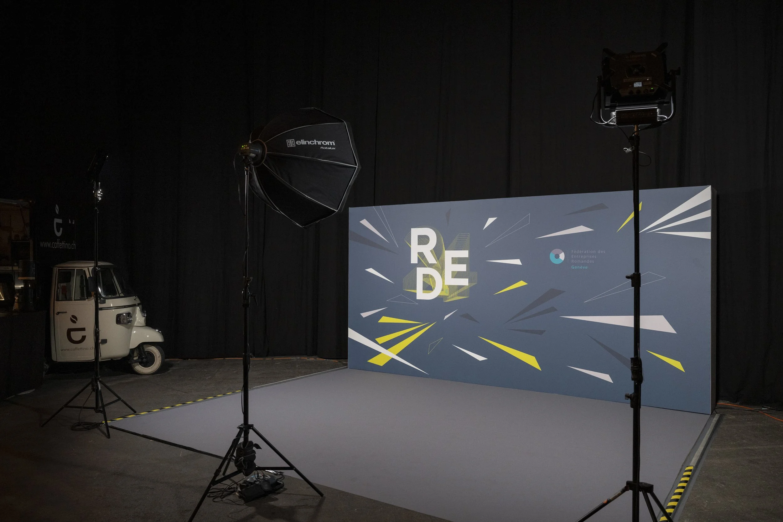 Une scène d'émission vidéo ou photo avec un fond d'écran bleu, une petite voiture électrique blanche et du matériel d'éclairage.