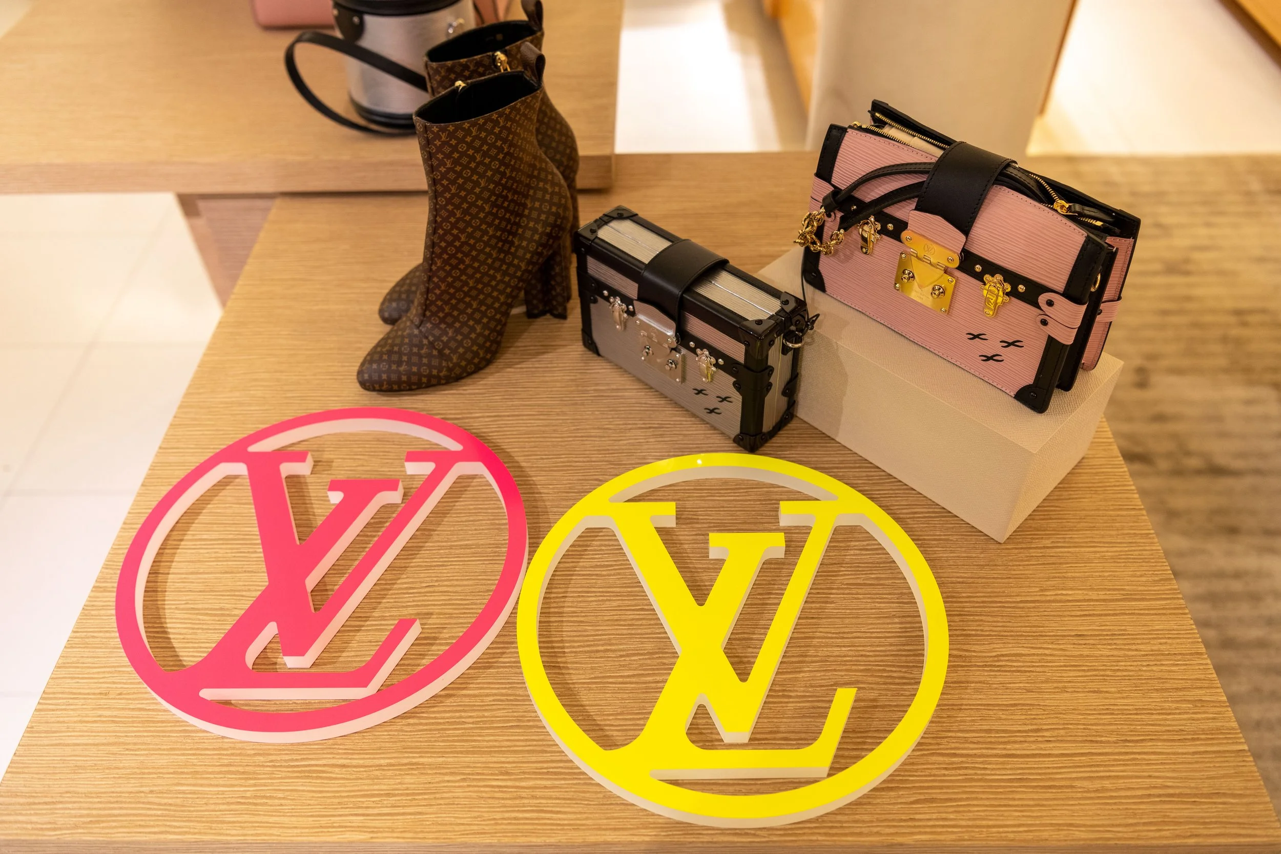 Deux sacs à main de marque Louis Vuitton, un bottillon en tissu à motif monogramme, deux logos Louis Vuitton en plastique (rose et jaune) en premier plan.