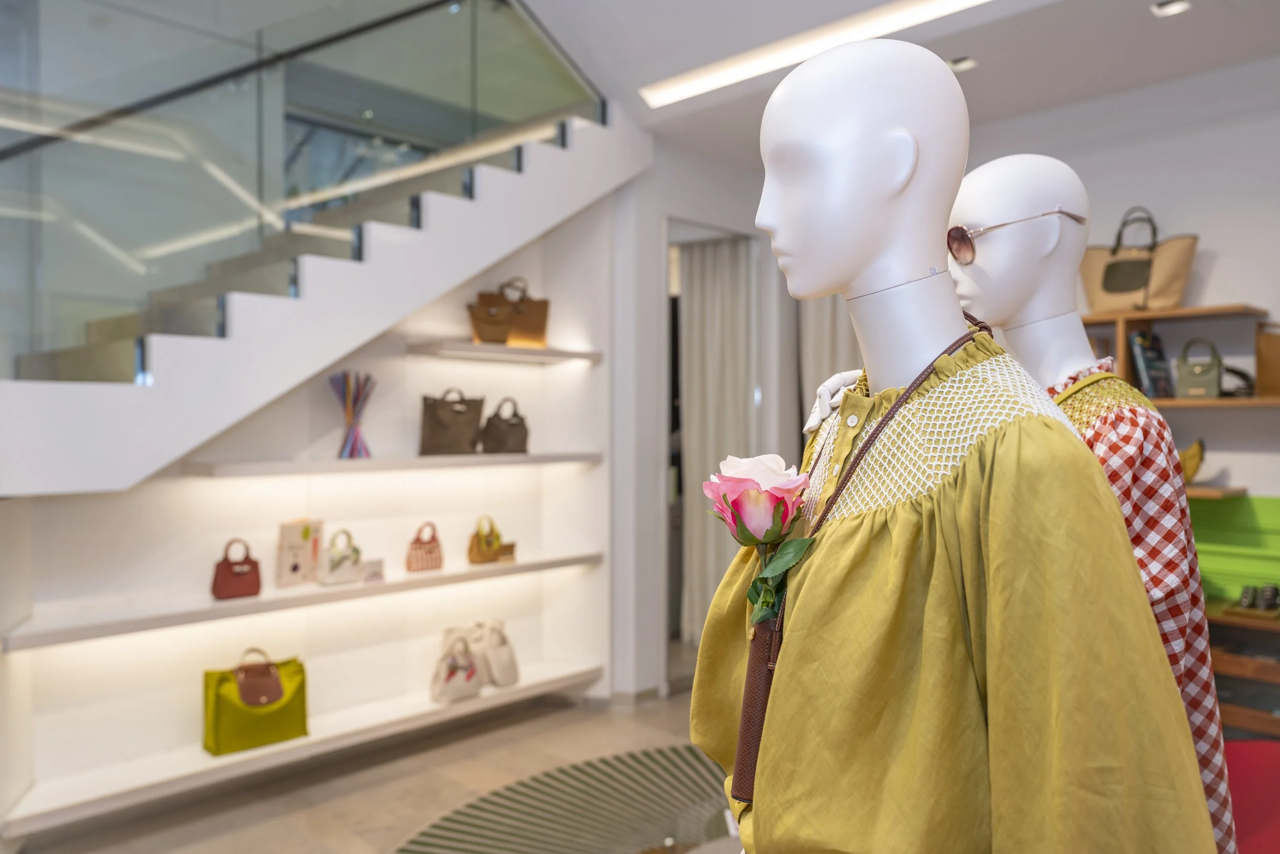 Mannequins avec vêtements dans une boutique de mode, décor moderne, étagères avec sacs à main en arrière-plan.