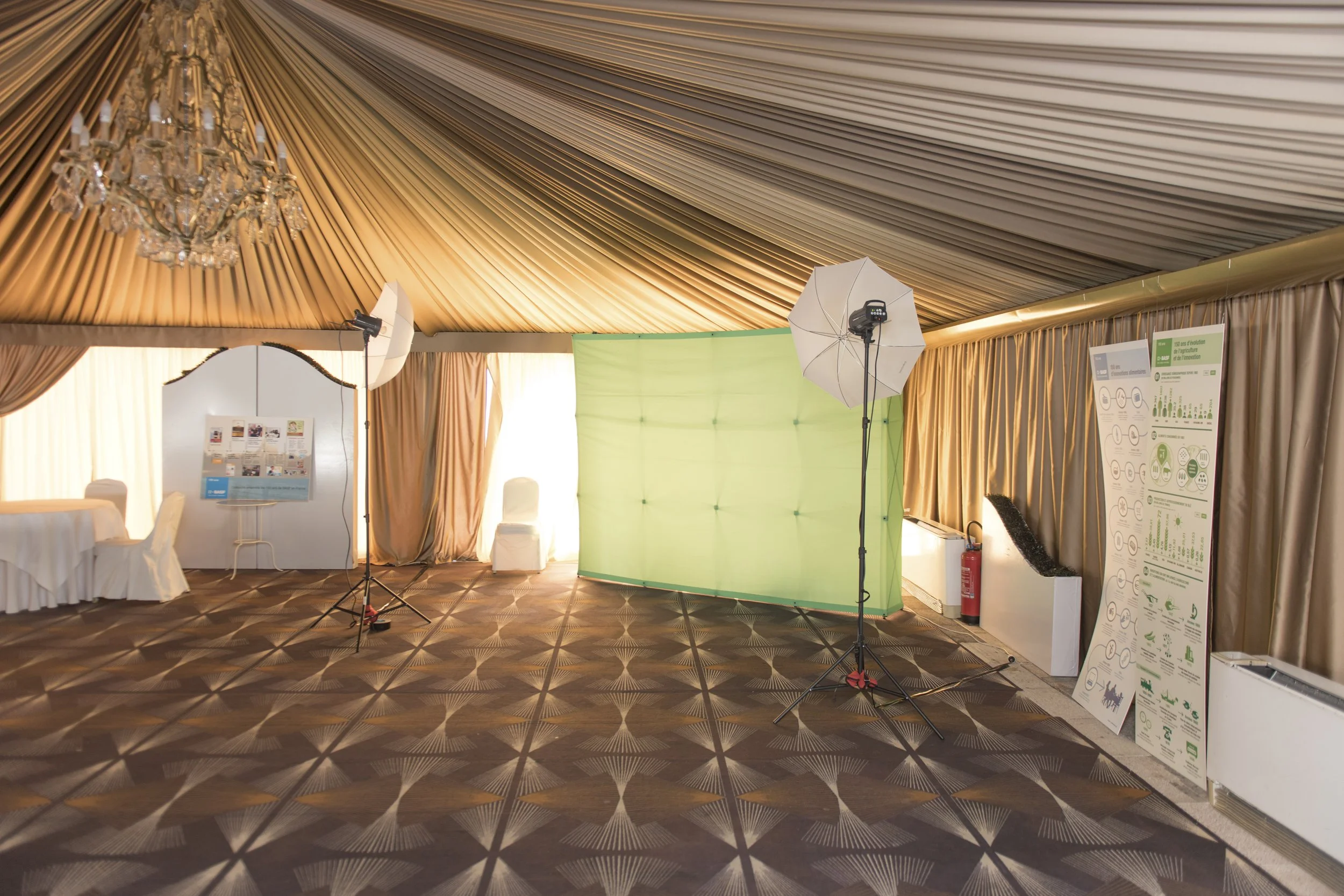 Espace de studio photo avec équipement d'éclairage professionnel, toile verte en arrière-plan, panneaux d'exposition et mobilier dans une salle décorée avec des rideaux en satin et un plafond drapé, pour une prise de photographie ou une présentation.