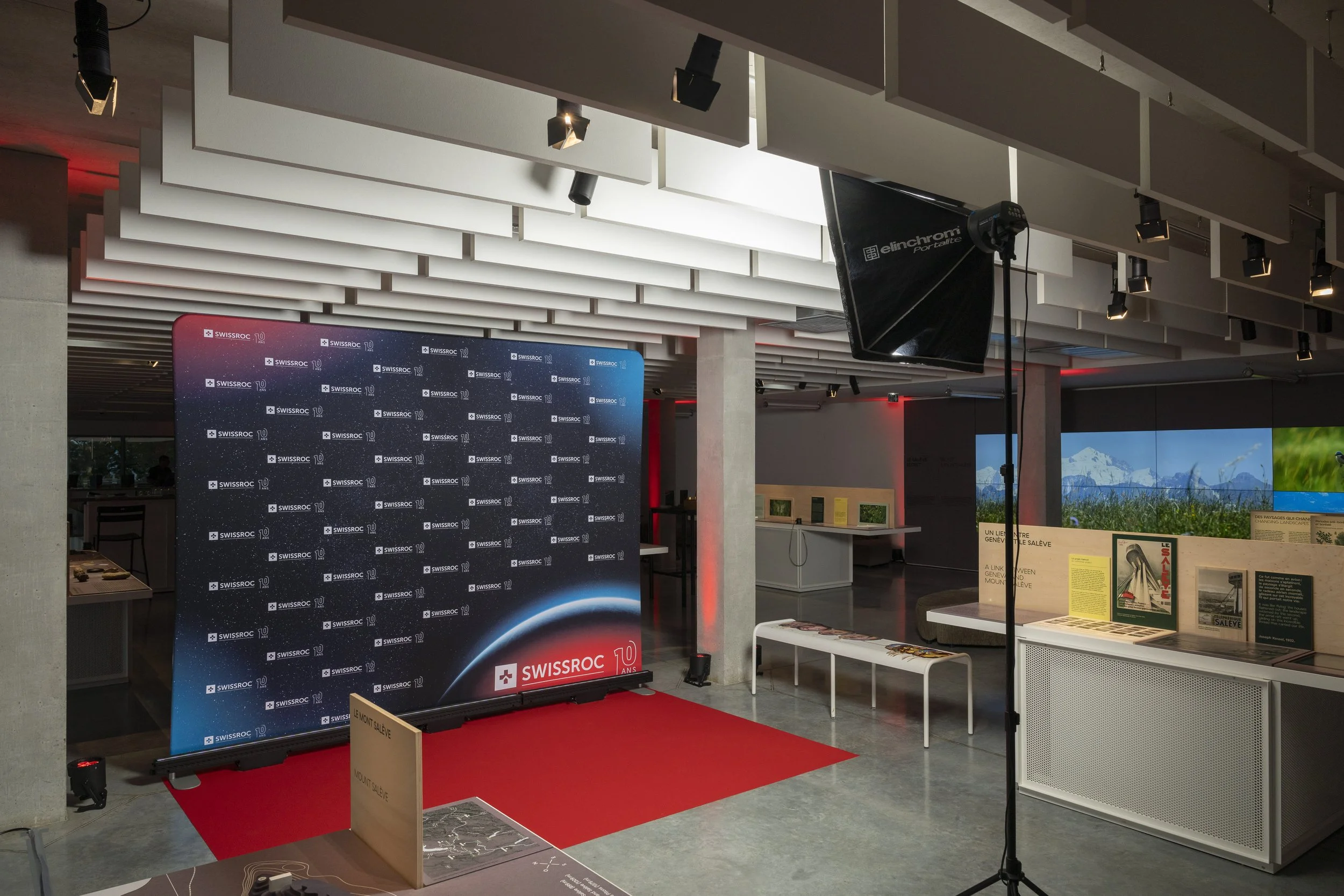 Une salle d'exposition ou d'événement avec un arrière-plan de marque Swissroc, un tapis rouge, un panneau de fond, des écrans et des affichages informatifs.