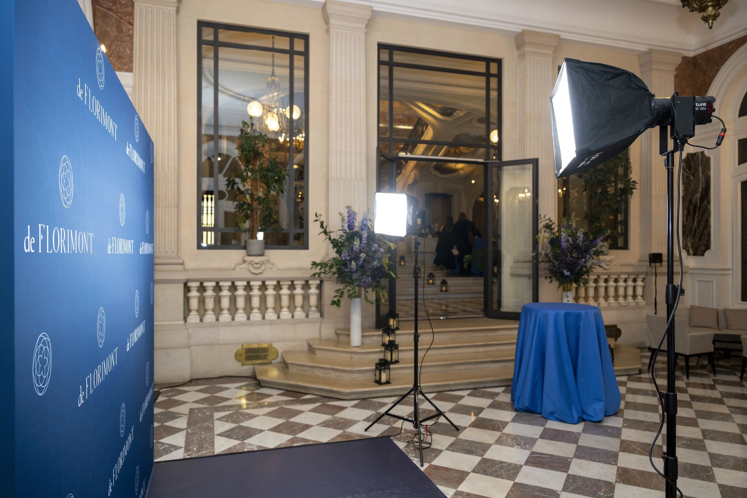 Studio de photographie avec éclairage professionnel, colonnes en marbre, escaliers, portes en verre, et décor floral dans une salle élégante.