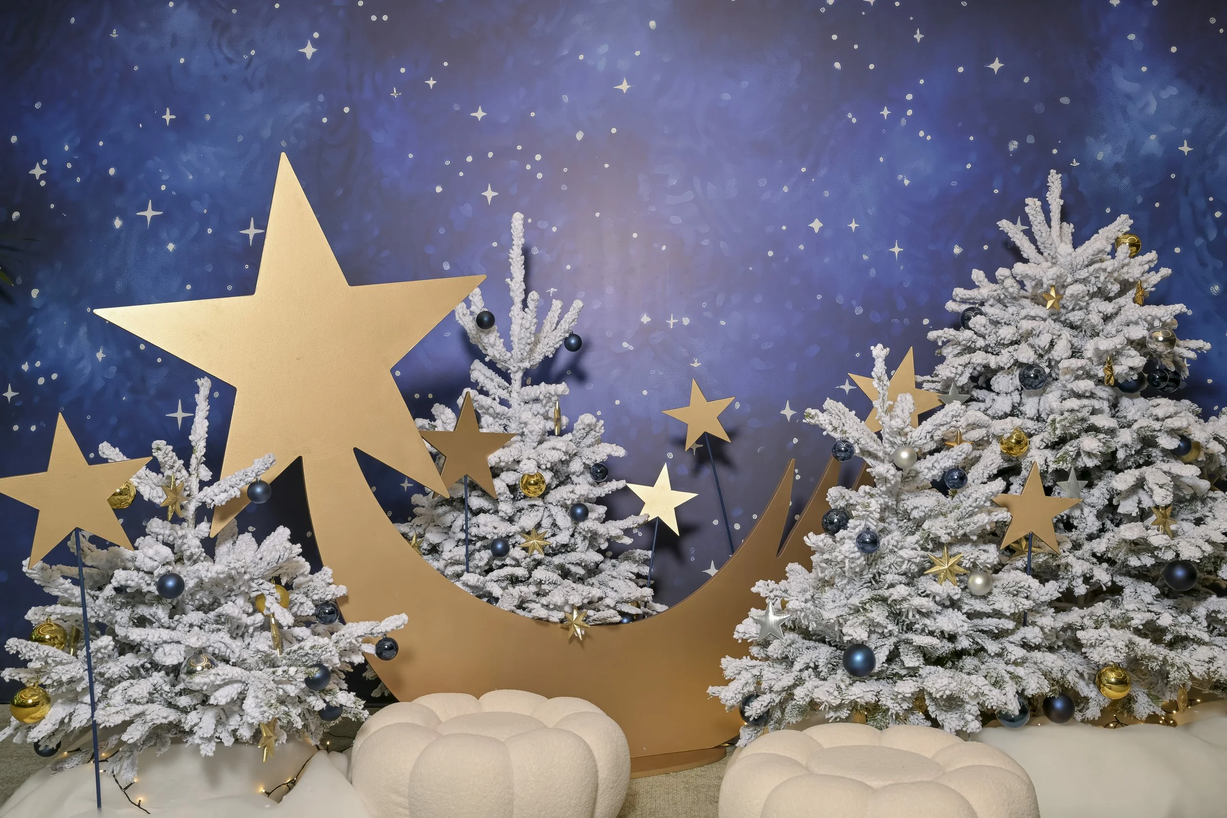 Décoration de Noël avec deux arbres enneigés décorés de boules dorées et bleues, un grand croissant en or avec des étoiles en or et en papier doré, sur un fond étoilé bleu.