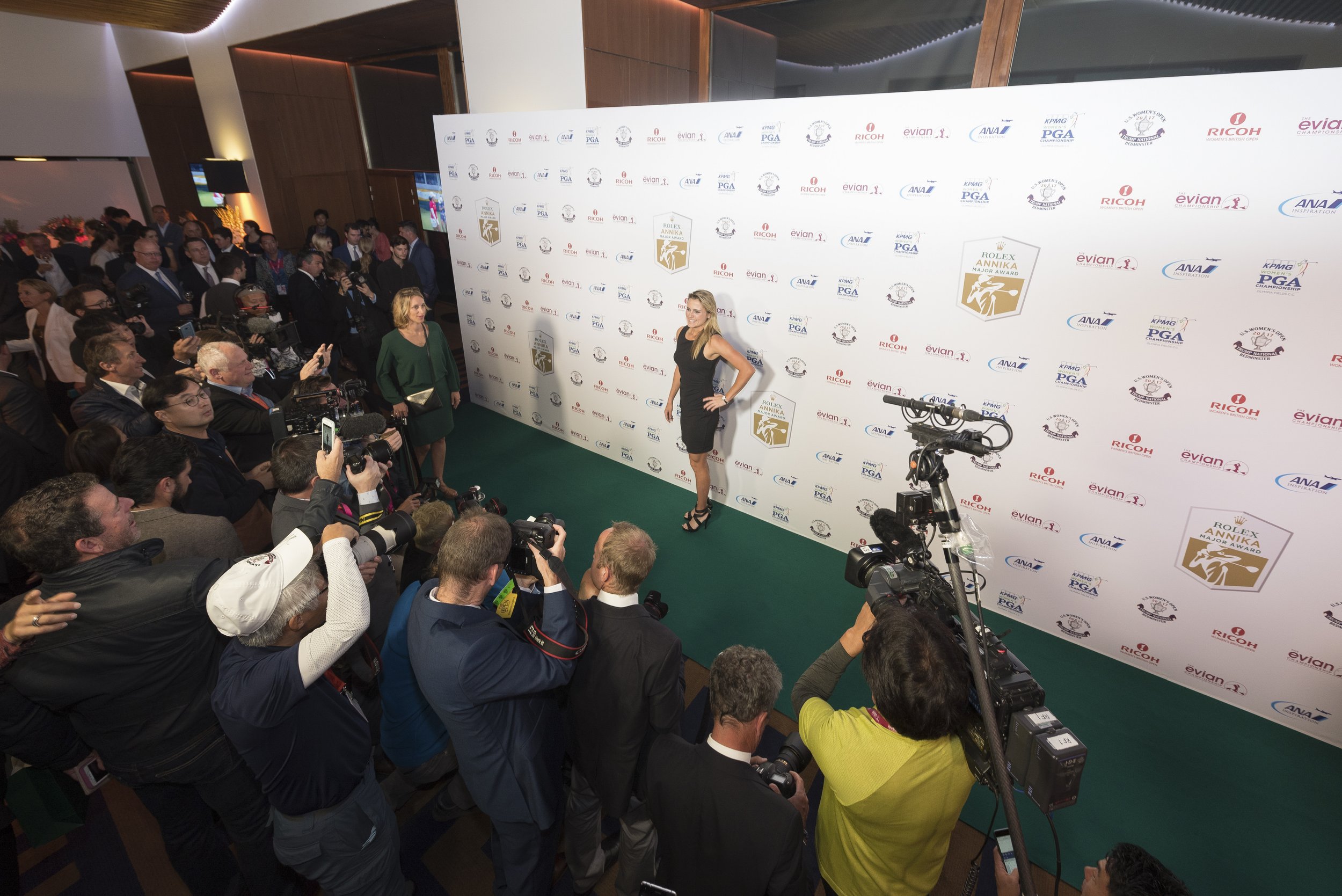 Cérémonie de remise de prix avec une femme en robe noire posant devant un mur de sponsors lors d'une soirée de gala.