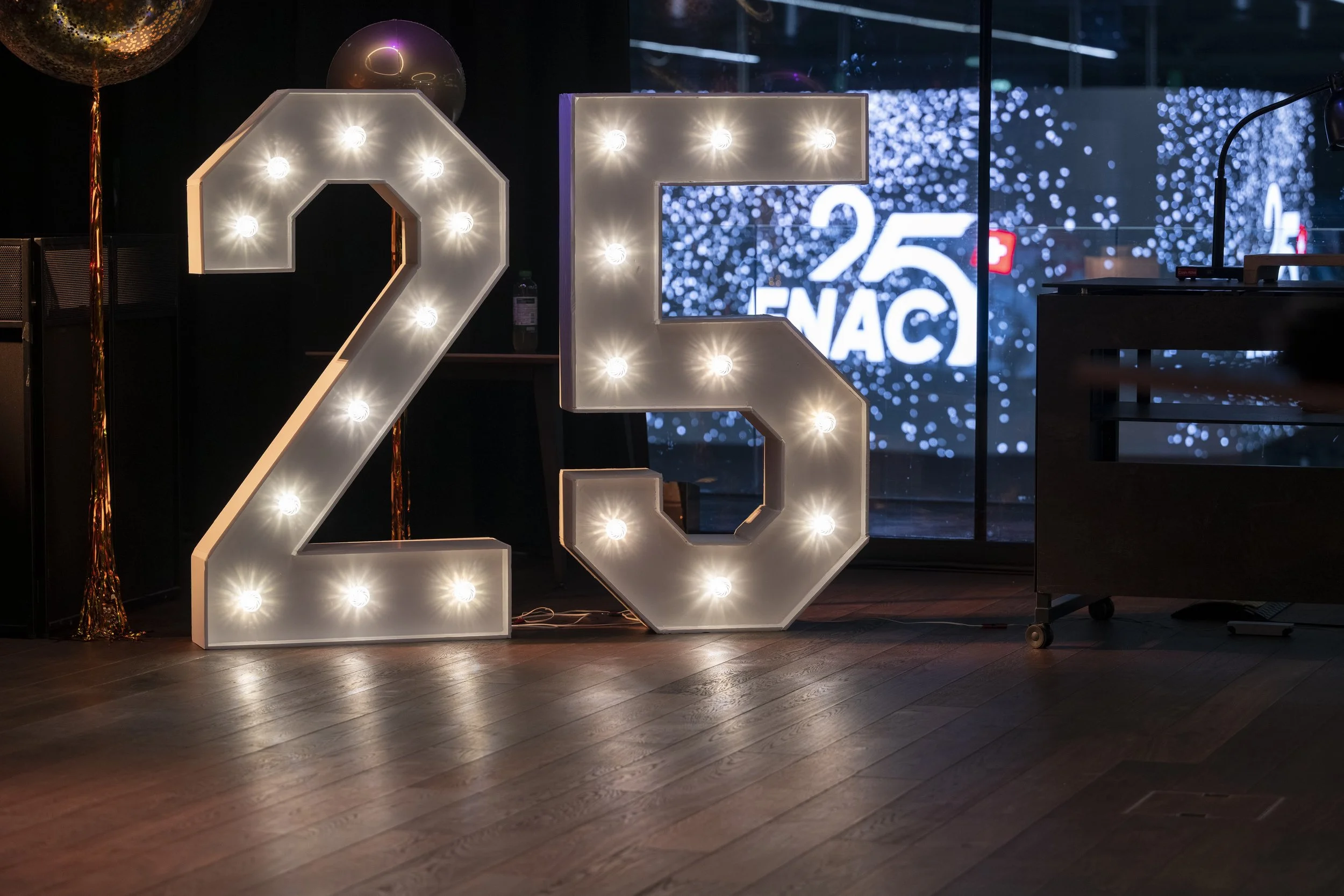 Décoration pour une fête d'anniversaire de 25 ans avec des chiffres lumineux 2 et 5, et un écran à l'arrière affichant '25 FNAC'