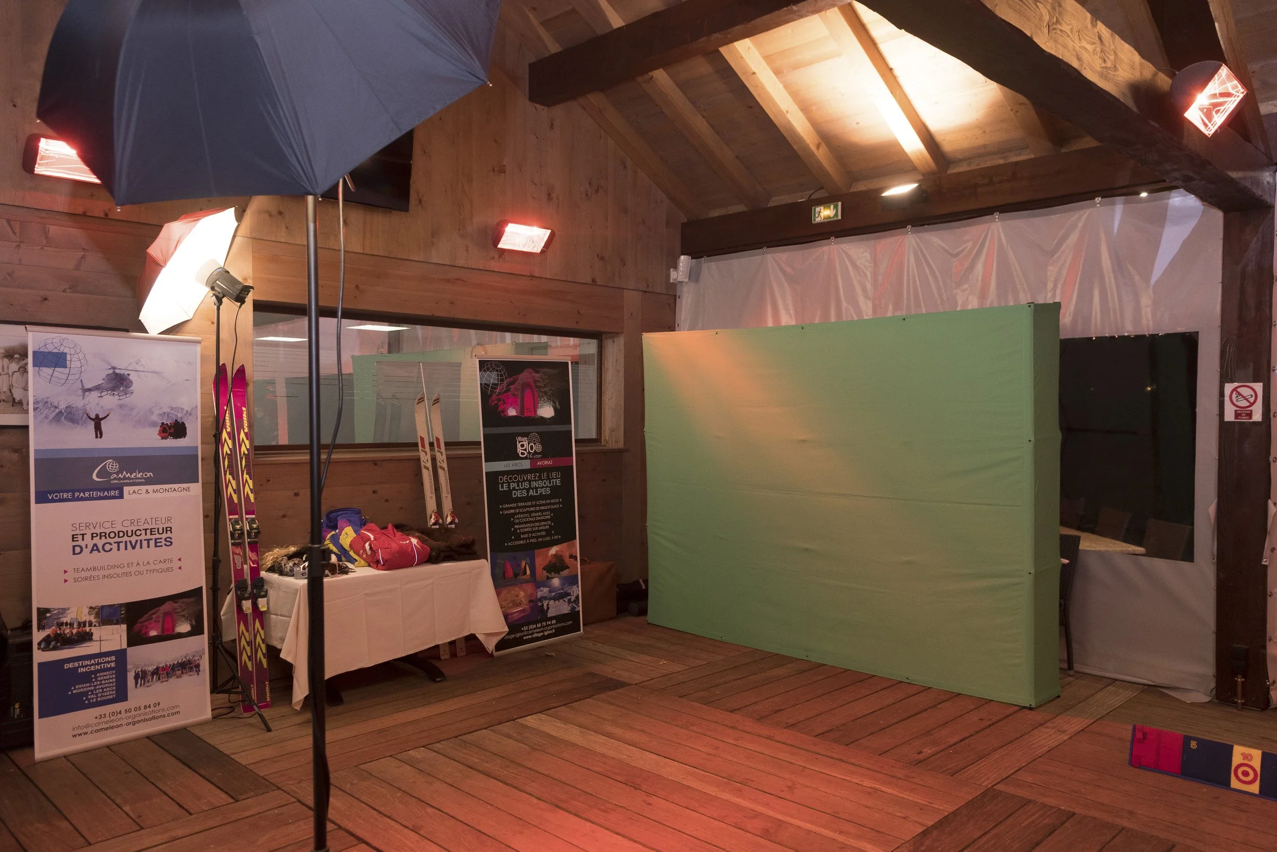 Une salle intérieure en bois avec des équipements de sports d'hiver, des affiches promotionnelles, des skis, et un mur vert pour fond vert, avec un éclairage chaud.