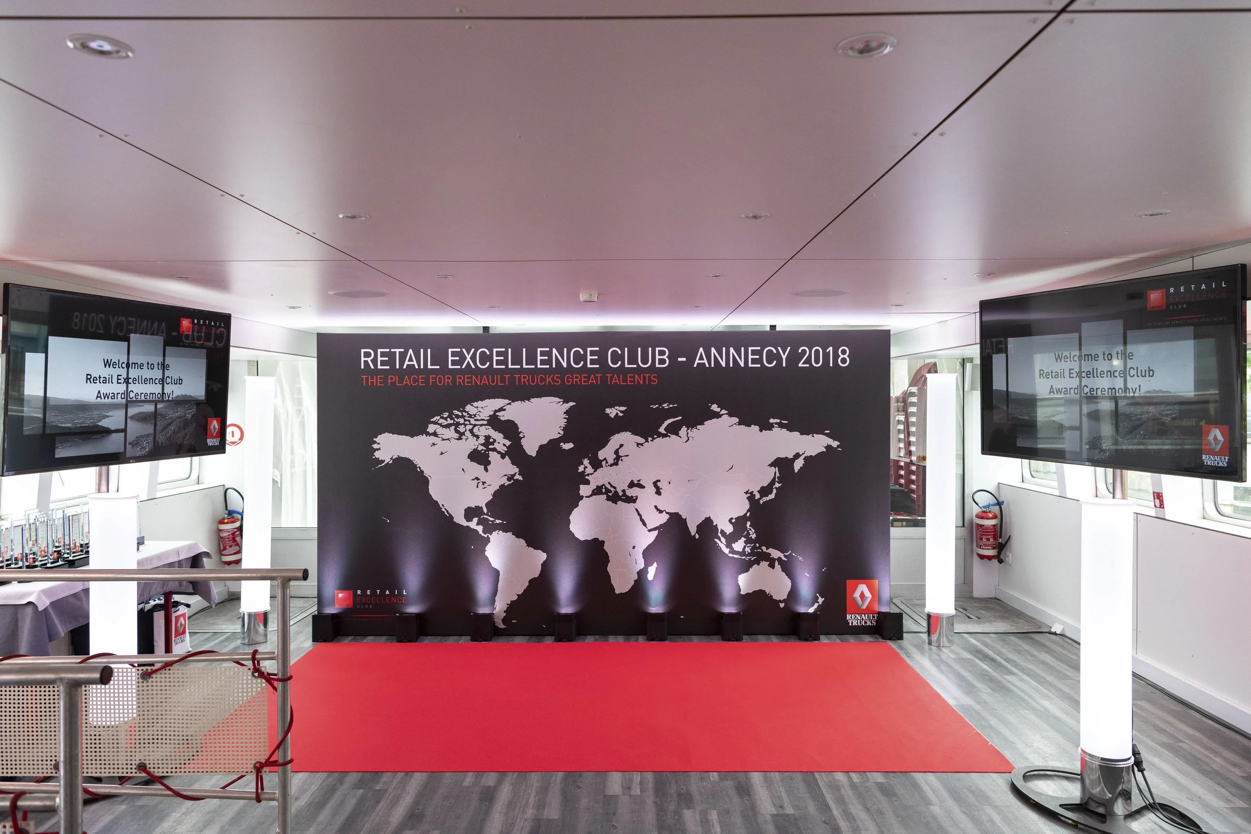 Espace d'accueil pour la cérémonie de remise des prix du Retail Excellence Club Annecy 2018, avec un grand panneau noir affichant un monde en blanc, le logo Renault Trucks et un tapis rouge.