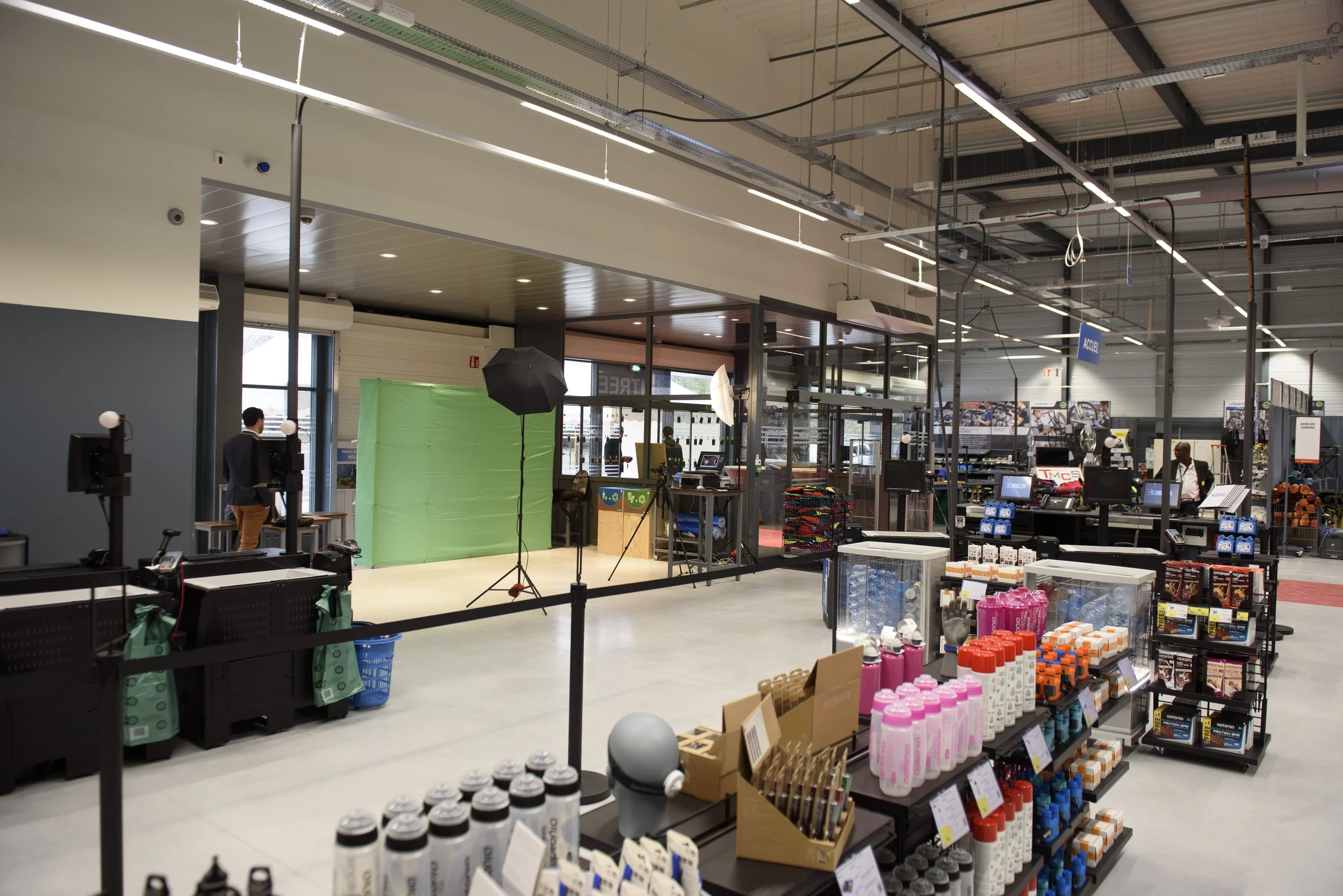 Une zone de studio photo installée dans un grand magasin avec un fond vert, des éclairages, et plusieurs caisses de produits de la boutique