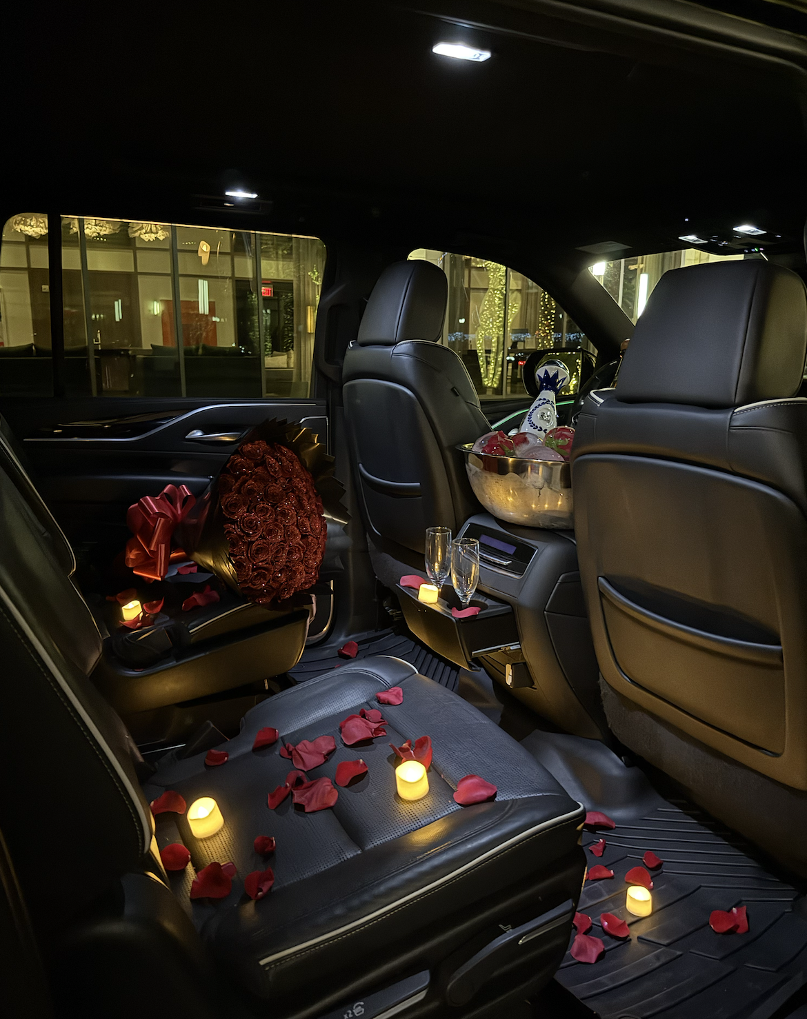 Car interior decorated with rose petals, candles, chocolates, and champagne glasses, suggesting a romantic setting.