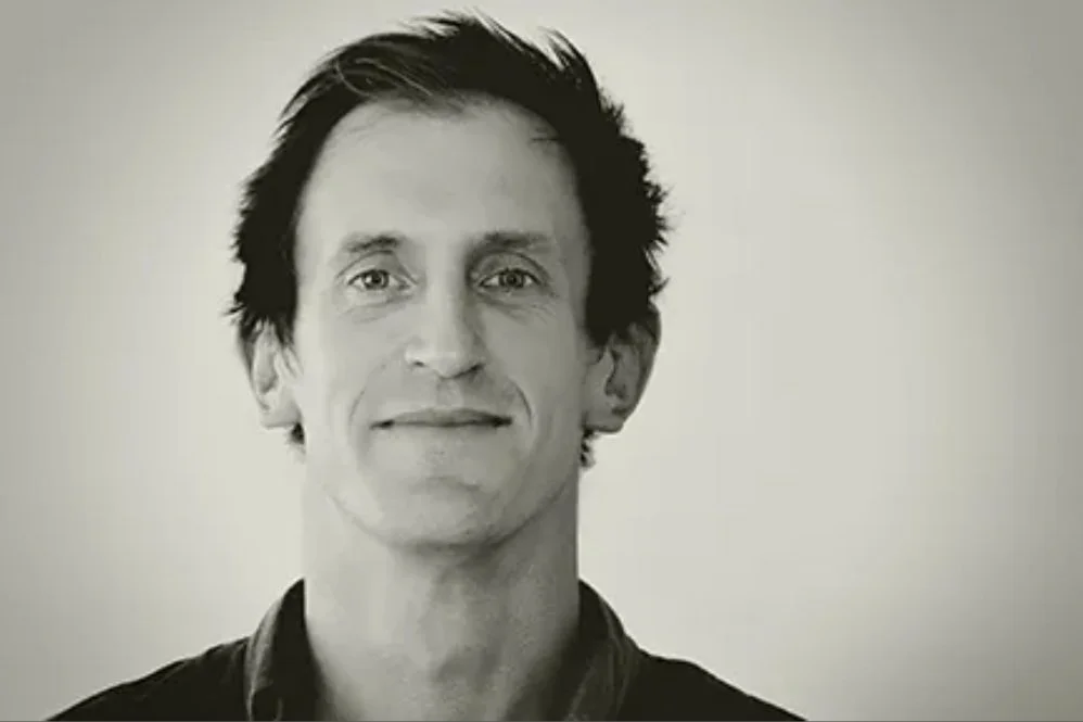 Black and white portrait of a smiling man with short, dark hair and a collared shirt, facing the camera against a plain background.