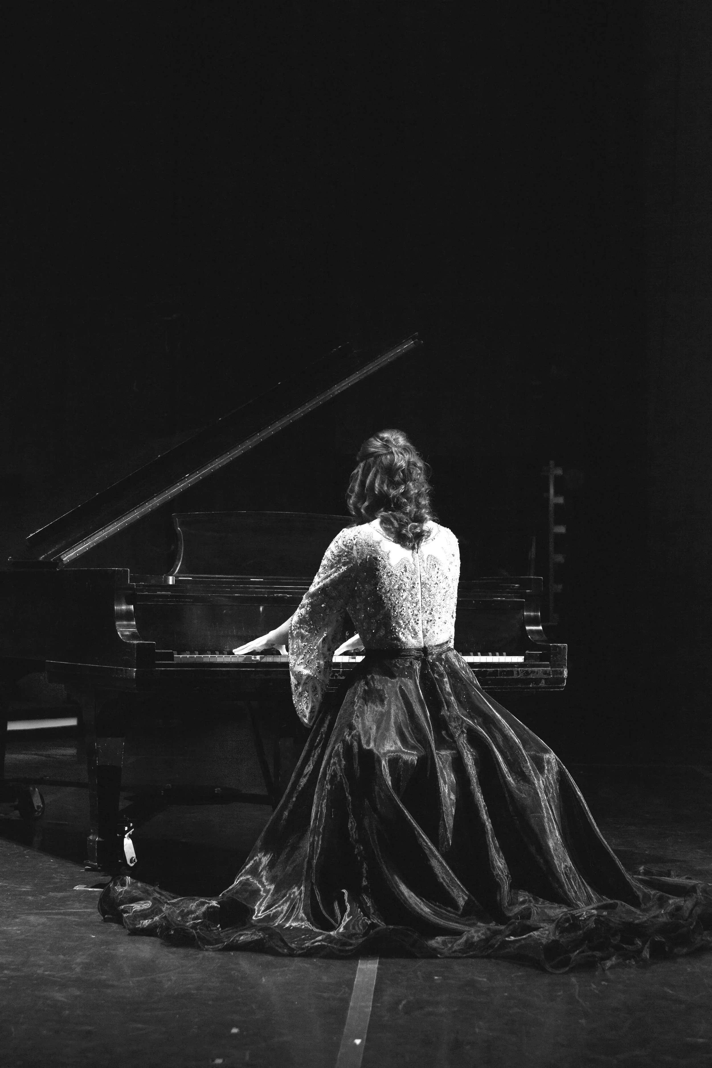 A woman in a long, elegant dress playing the piano on stage.