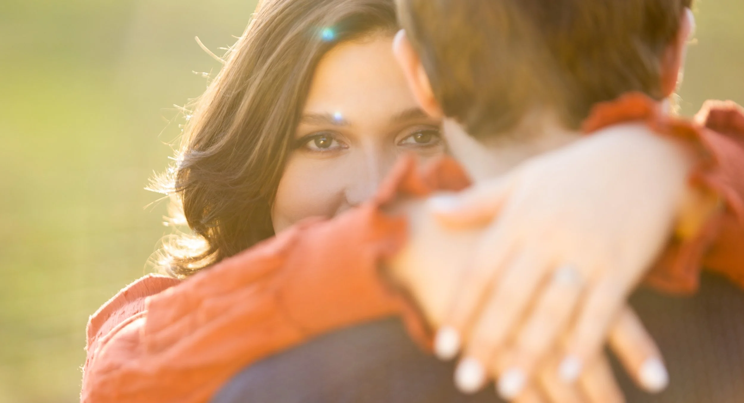 A woman gazes into the eyes of a man who is facing away, with sunlight in the background.
