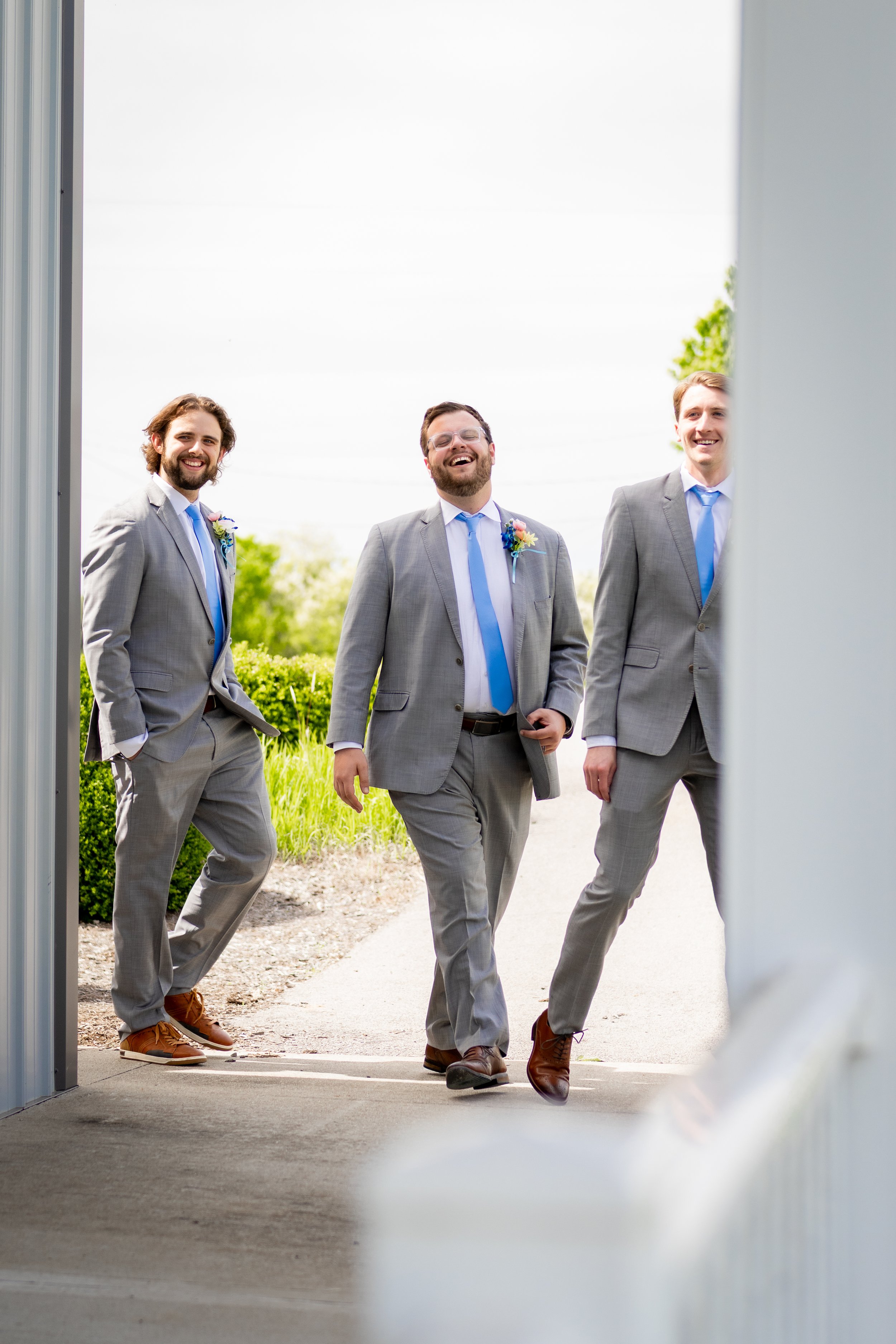 Three men in gray suits with blue ties walking outside, smiling and laughing.