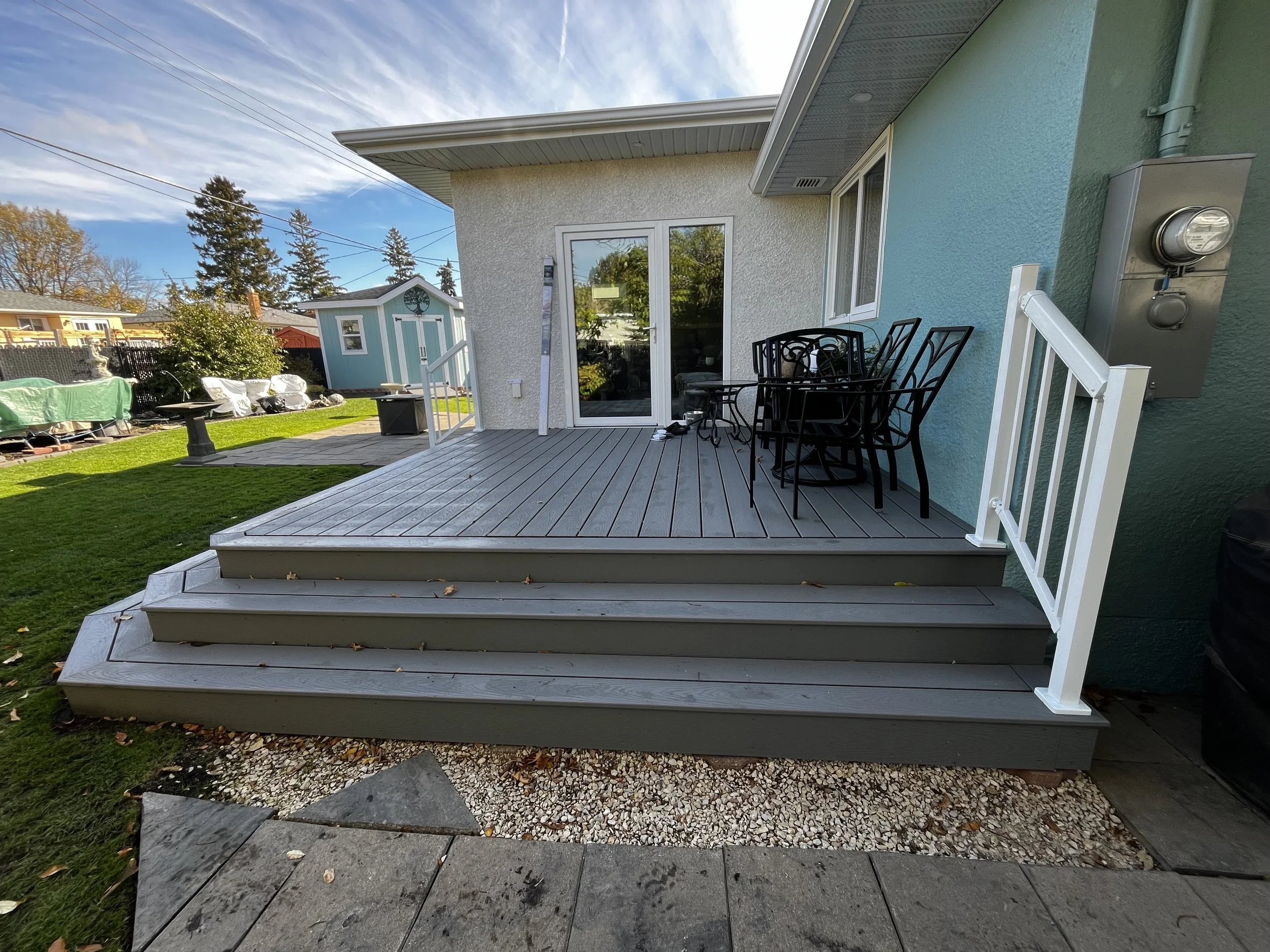 Backyard patio with stairs, black outdoor table and chairs, sliding glass door, and green lawn.