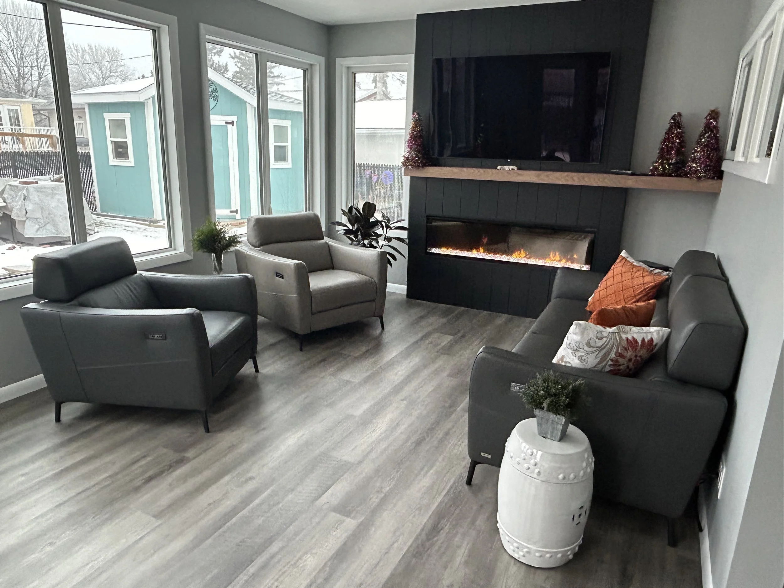 Living room with large windows, modern furniture, a wall-mounted flat-screen TV, a fireplace, and holiday decorations.
