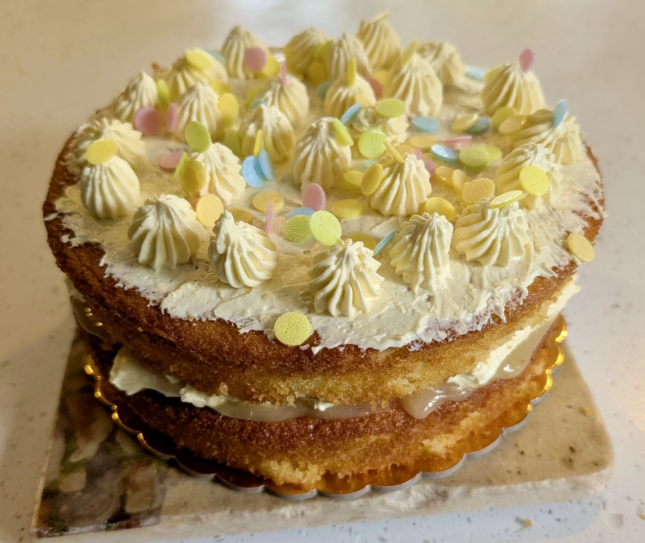 A birthday cake decorated with yellow, pink, and blue confetti, topped with small dollops of white frosting.