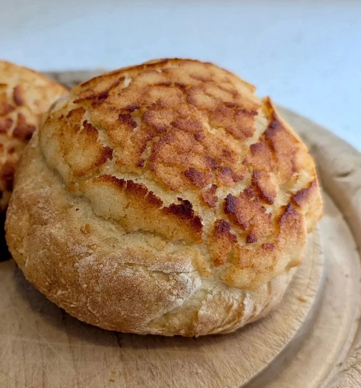 Close-up of a freshly baked bread roll with a golden, crispy crust and a cracked surface on a wooden surface.