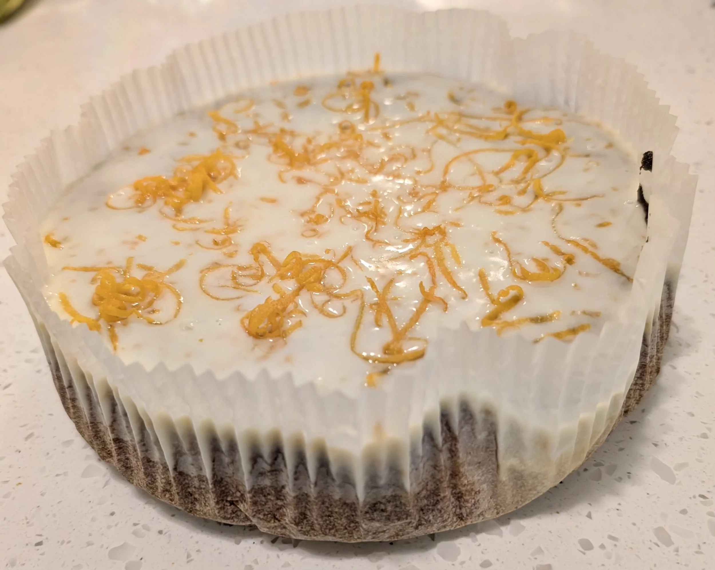 Cupcake with white frosting and orange sprinkles in a white paper cupcake liner on a light-colored surface.
