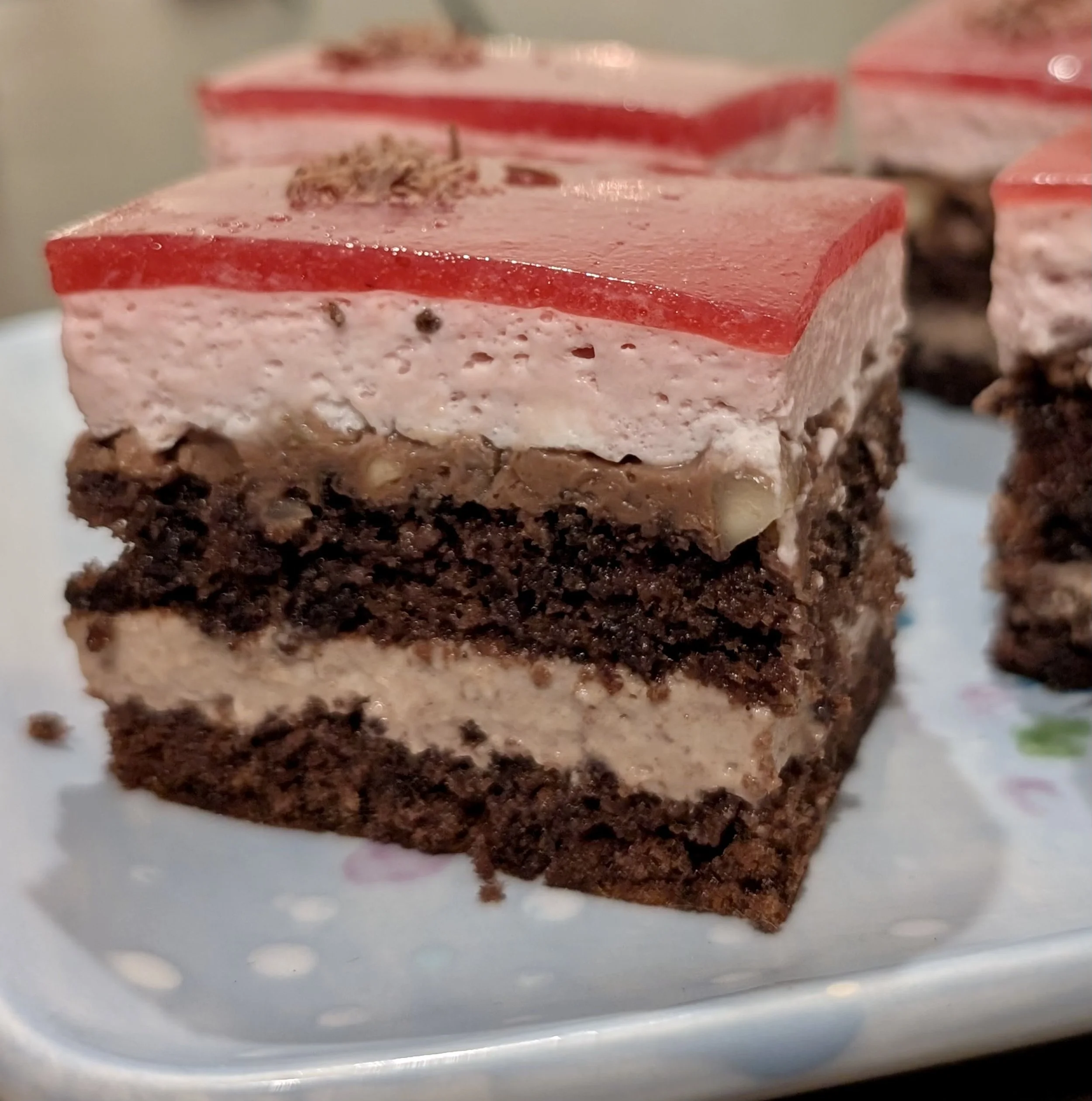 Close-up of a layered dessert with pink, white, and brown layers, topped with small sprinkles of brown.