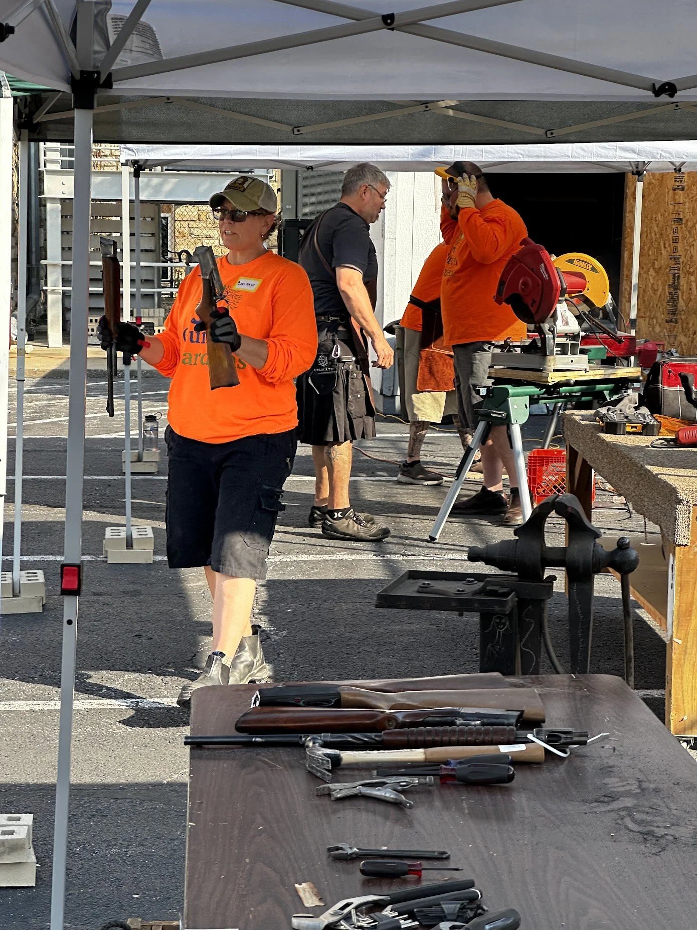 People working at a construction or renovation site under a tent, with tools and equipment visible on a table in the foreground.
